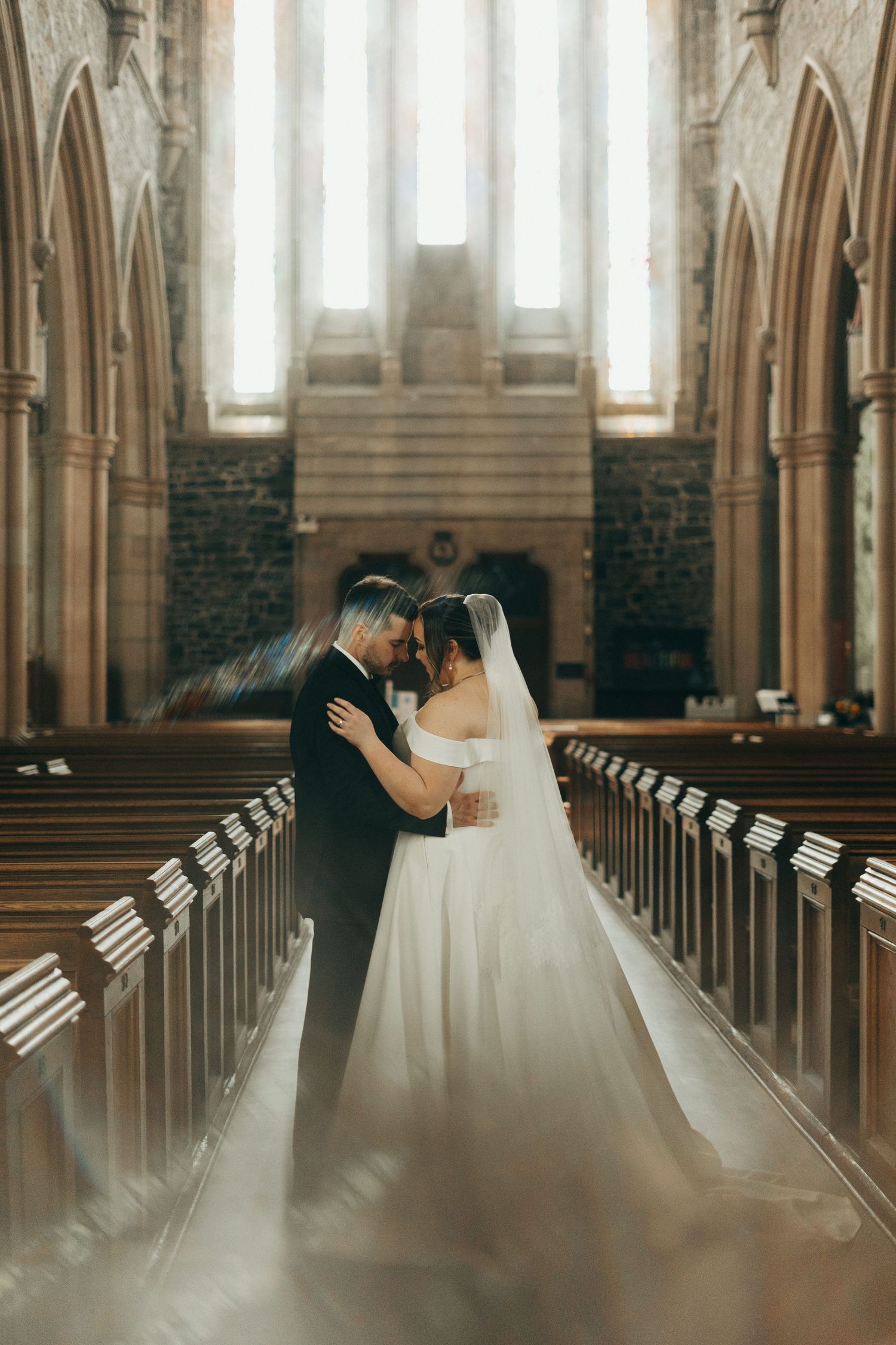 Wedding couple embracing in a grand cathedral aisle with gothic arches and natural light.