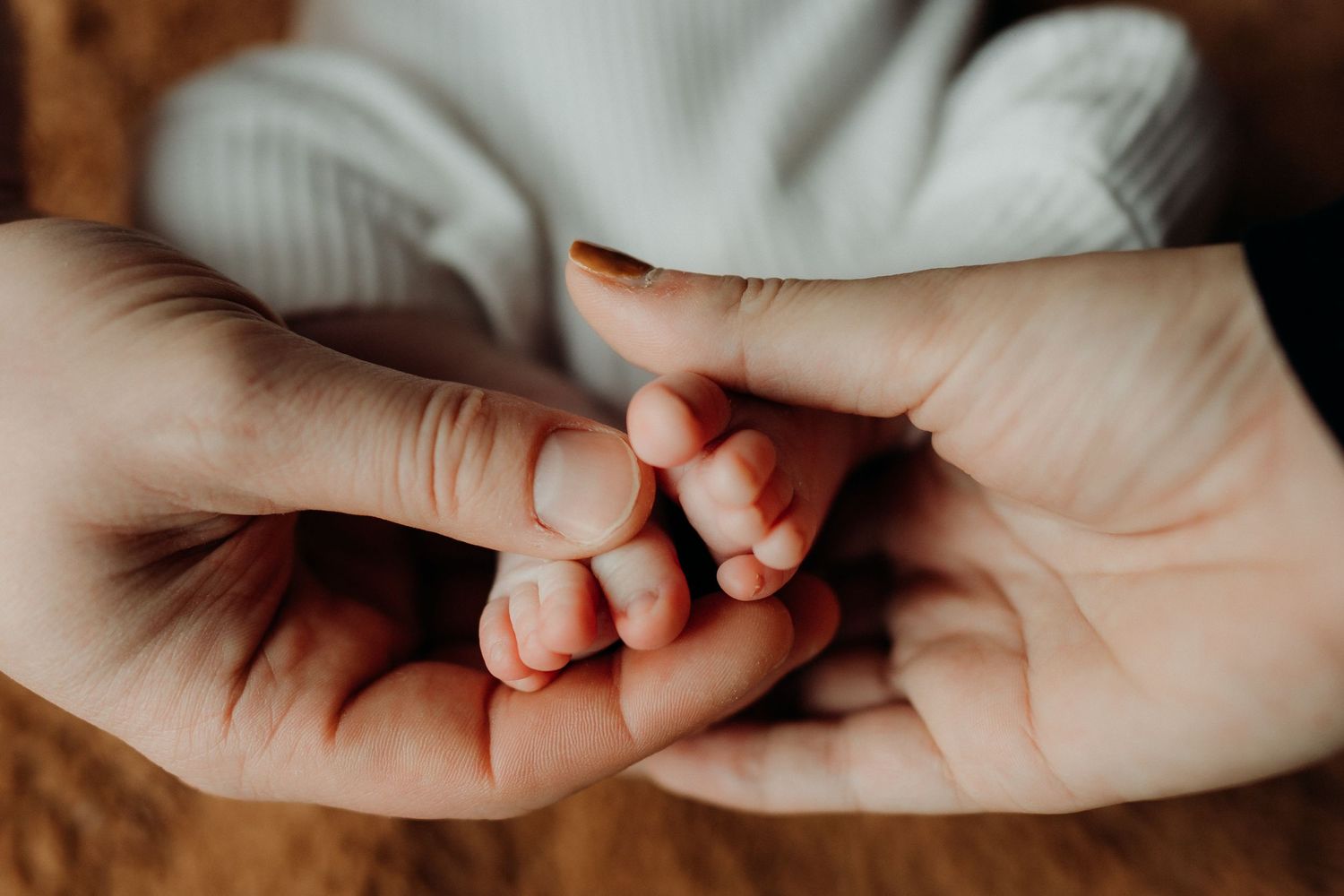 Delicate newborn baby fingers wrapped in caring hands against a dark background.