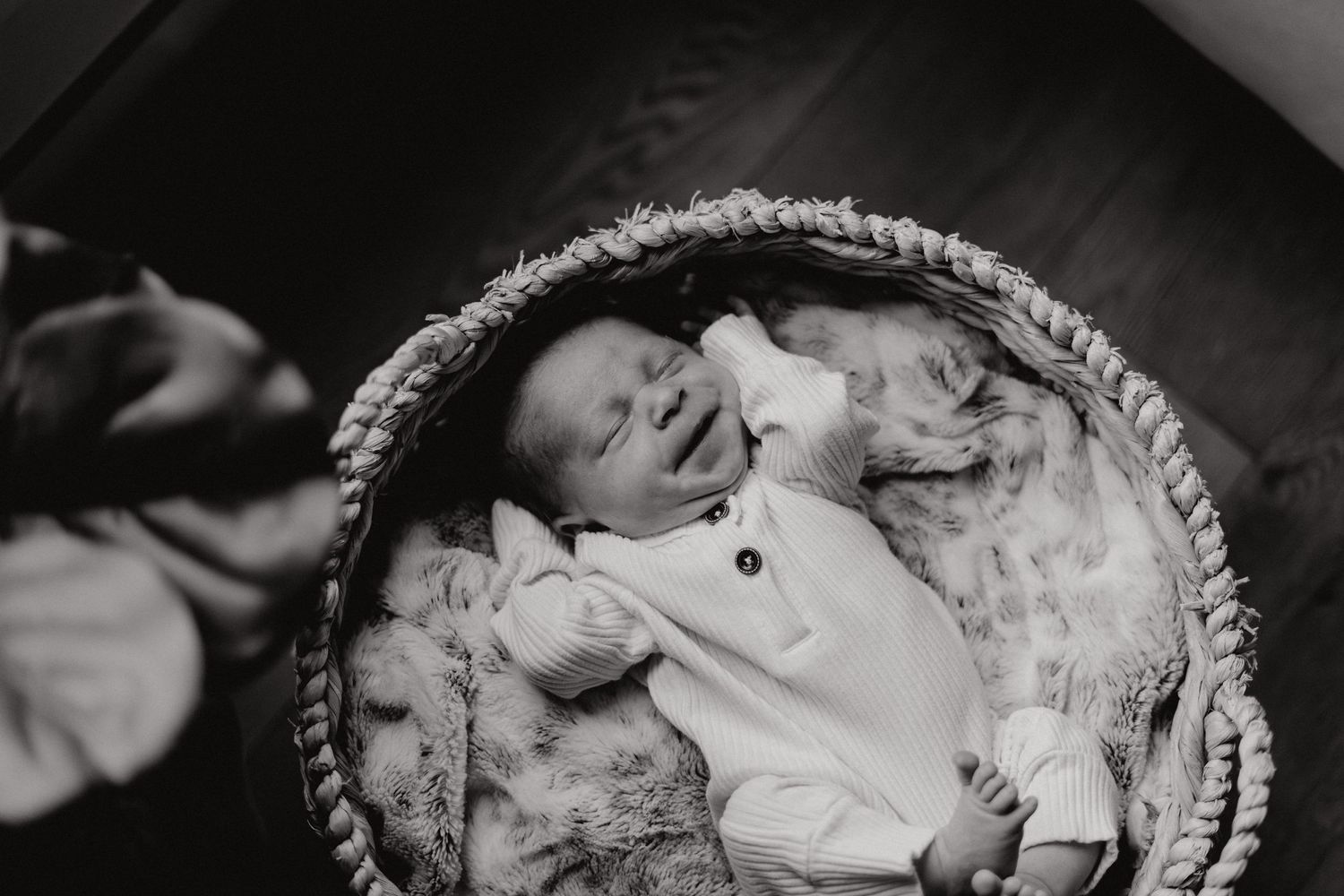 Black and white portrait of infant sleeping in rustic basket.