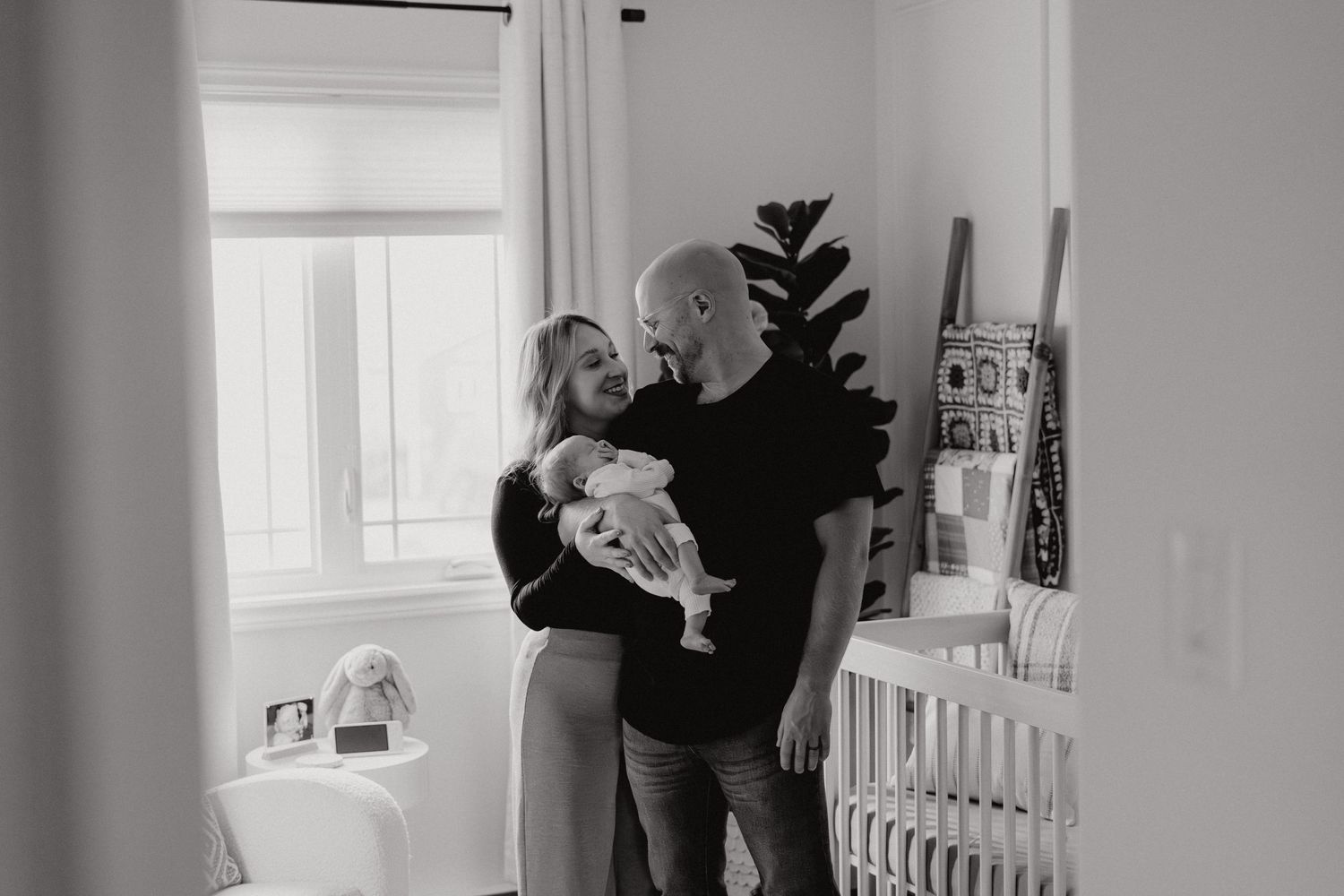 Black and white capture of family bonding in nursery with natural light.