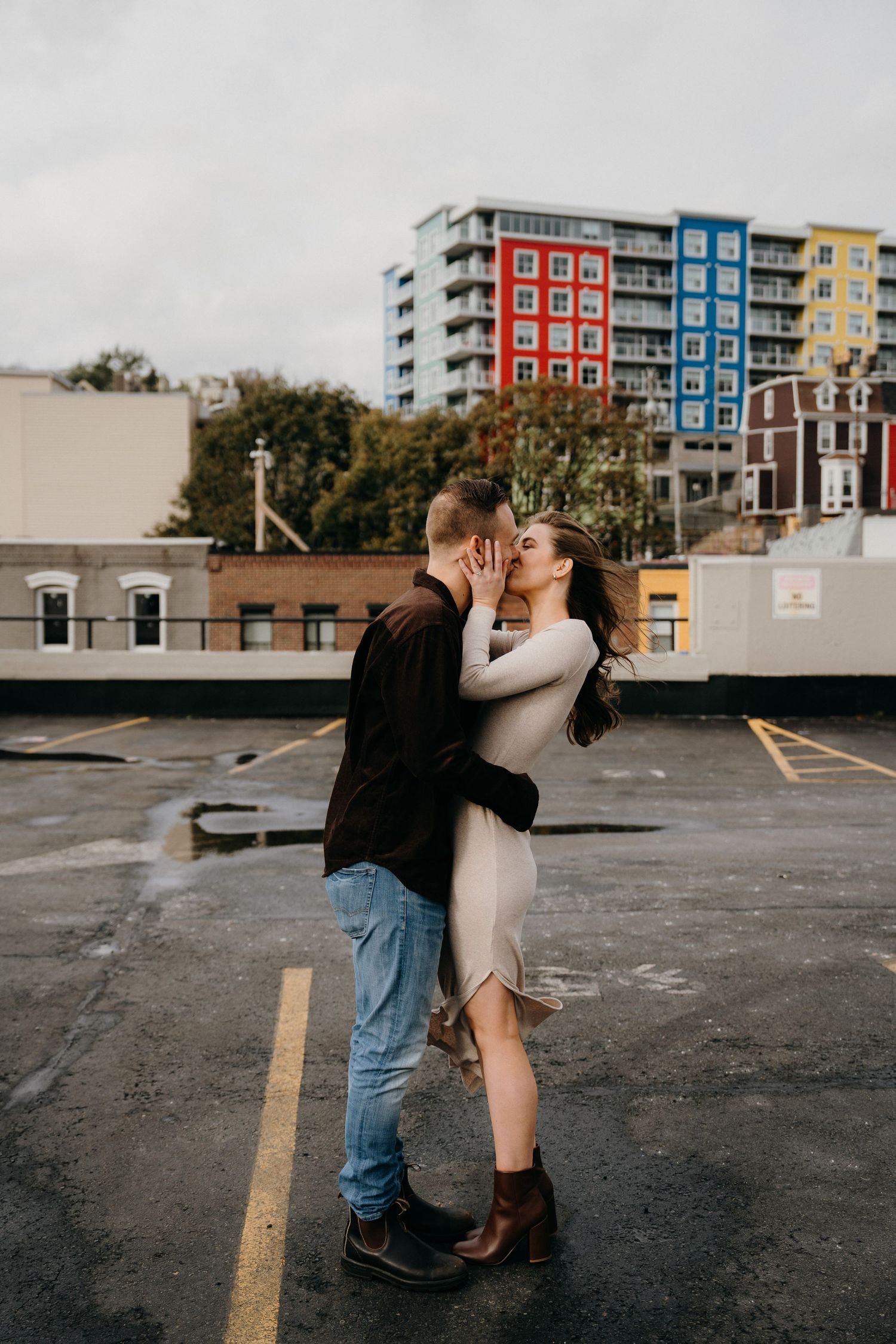 A couple shares an intimate dance in a parking lot with colorful architecture in view.