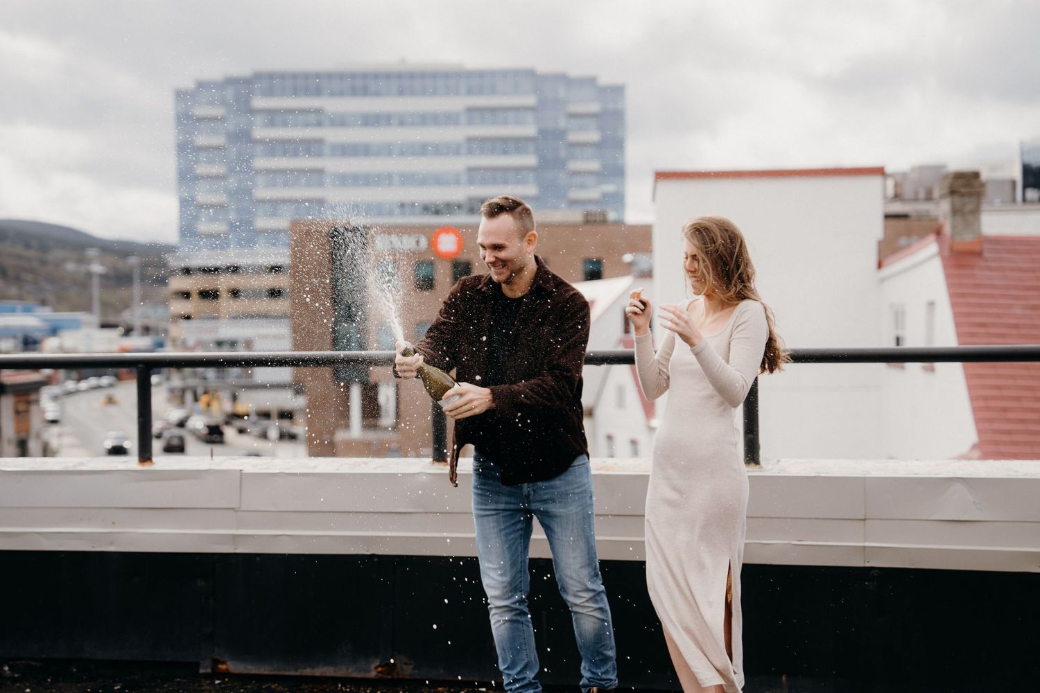 A romantic moment captured on a city rooftop with modern buildings visible in the distance.