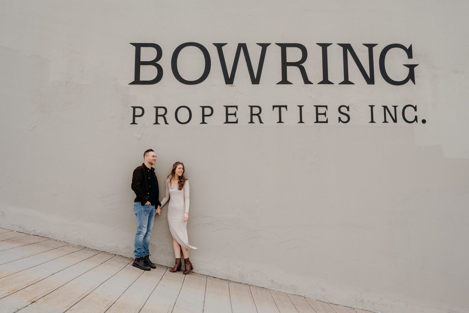 A romantic photoshoot featuring a couple near a wall with Bowring Properties signage.