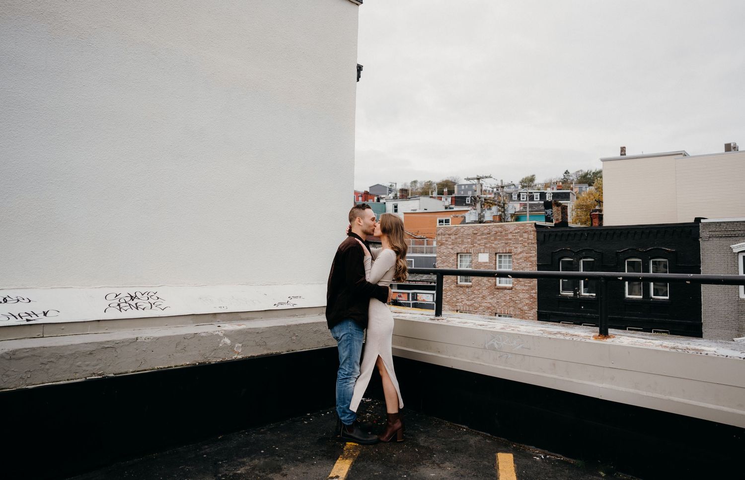 A couple embracing on a rooftop terrace with an urban cityscape behind them.