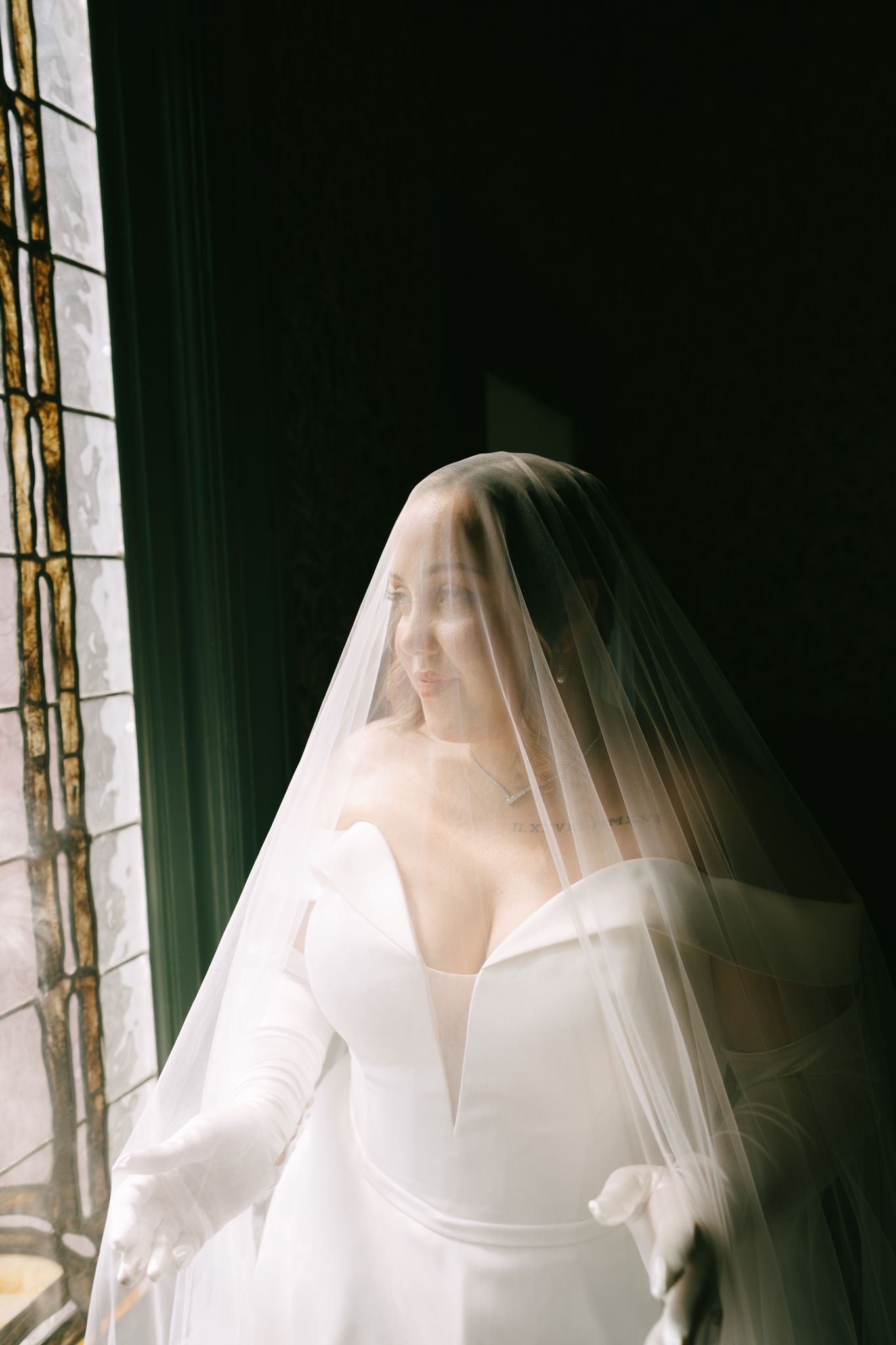 Wedding veil creates ethereal effect against stained glass window backdrop.