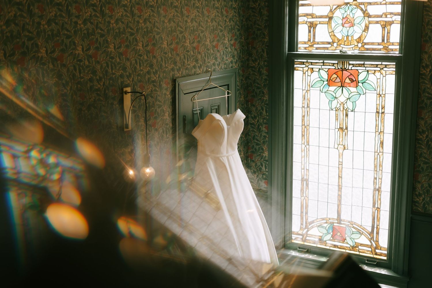 Stained glass windows create dramatic lighting in a historic room with patterned wallpaper.