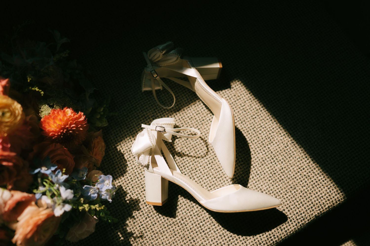 Wedding shoes and floral bouquet artistically photographed in dramatic shadows.