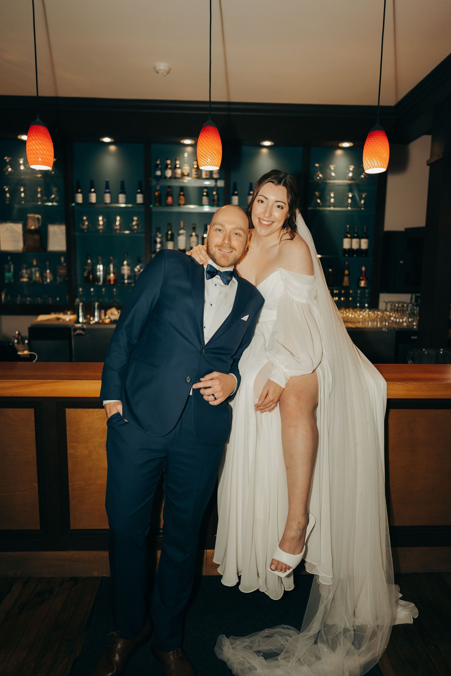 A bride and groom share joyful candid moments at their wedding reception bar area in warm lighting.