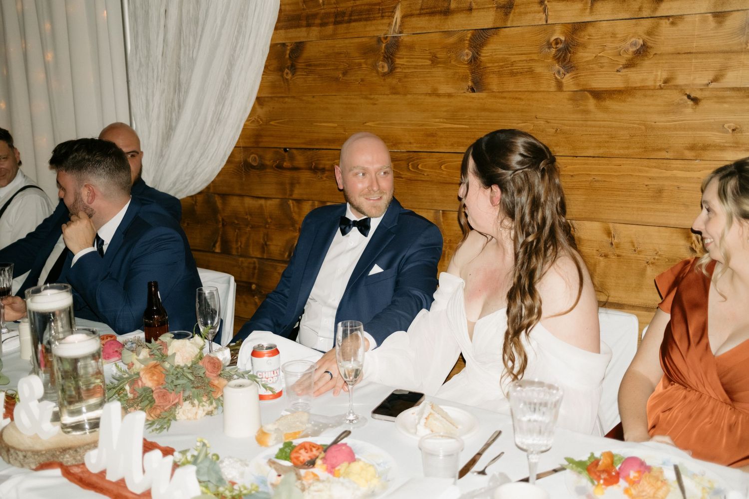 Wedding guests enjoy dinner at a rustic wooden table during an intimate reception celebration.