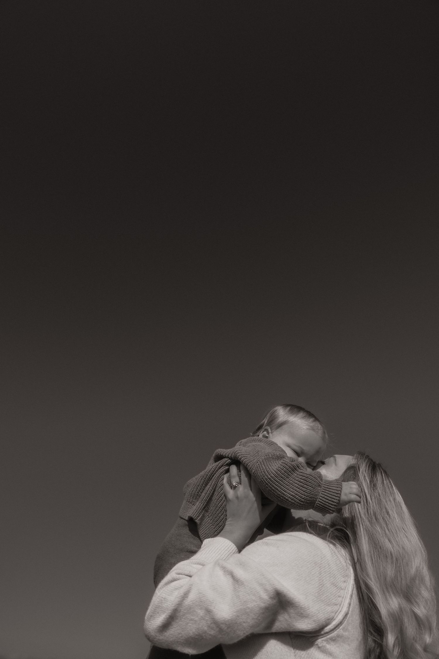 Black and white photograph of two people in an intimate embrace with their faces close together against a dark background.