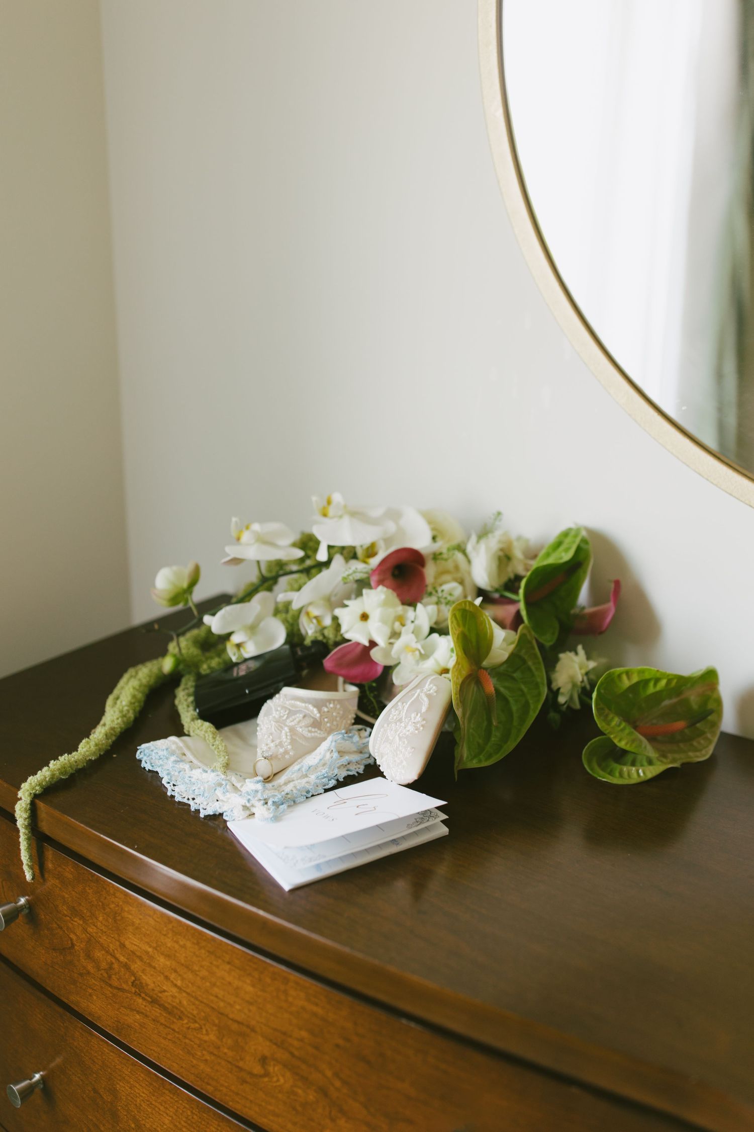 Floral arrangement with white and pink flowers on a wooden dresser beside a round mirror.