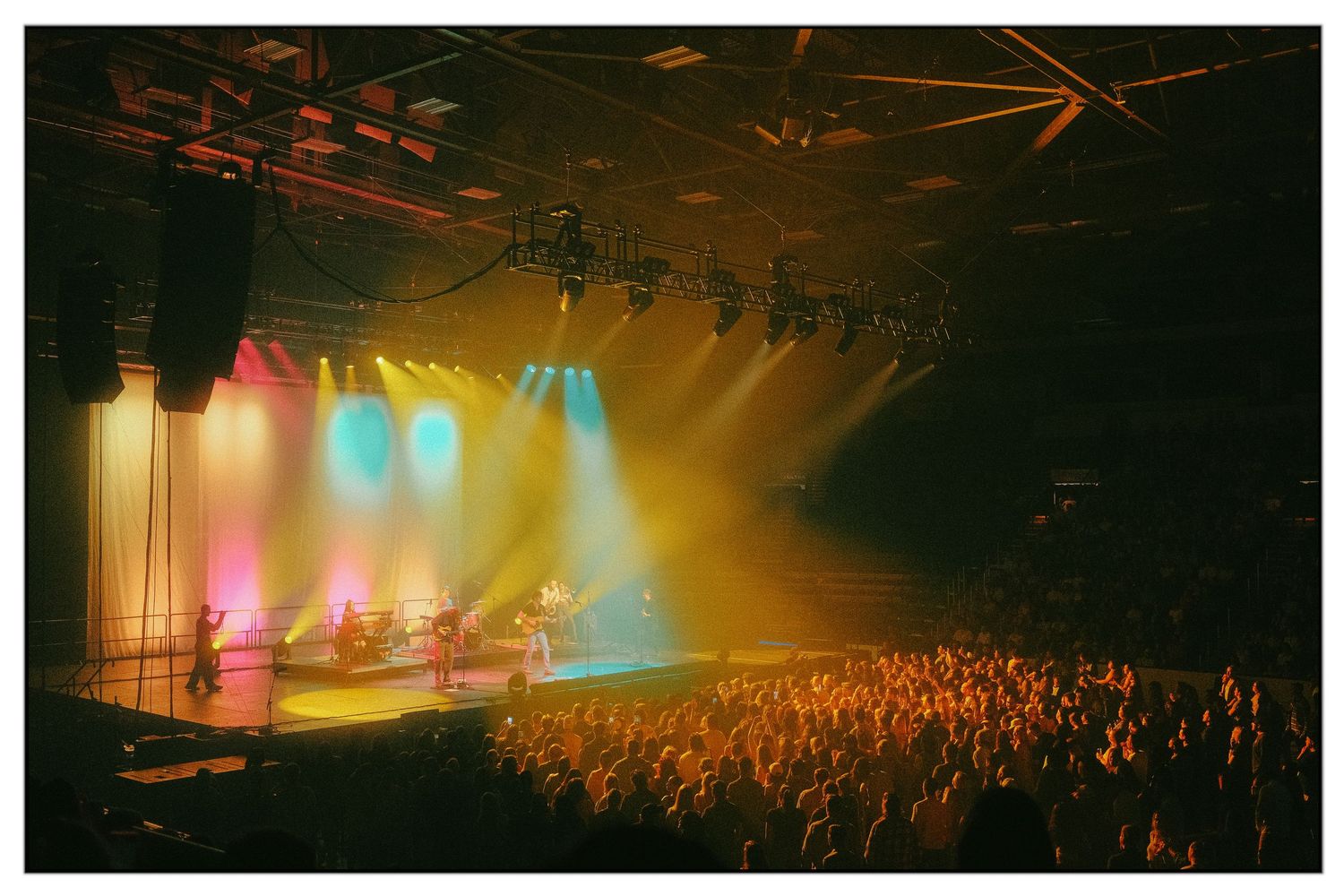 Concert crowd silhouettes illuminated by colorful stage lights during a live performance at a music venue.