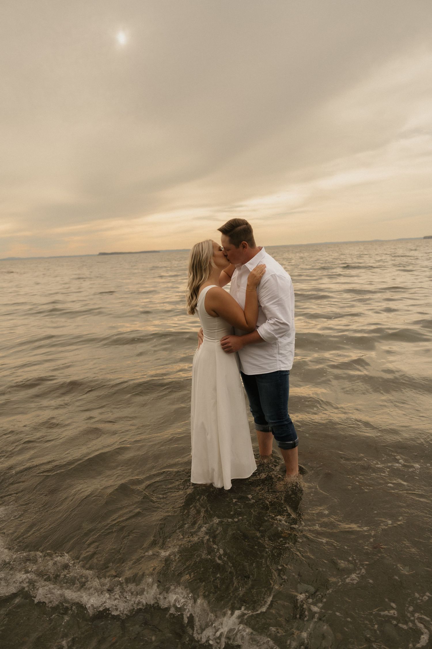 A romantic couple shares an intimate moment while standing in the ocean waves during a golden sunset.