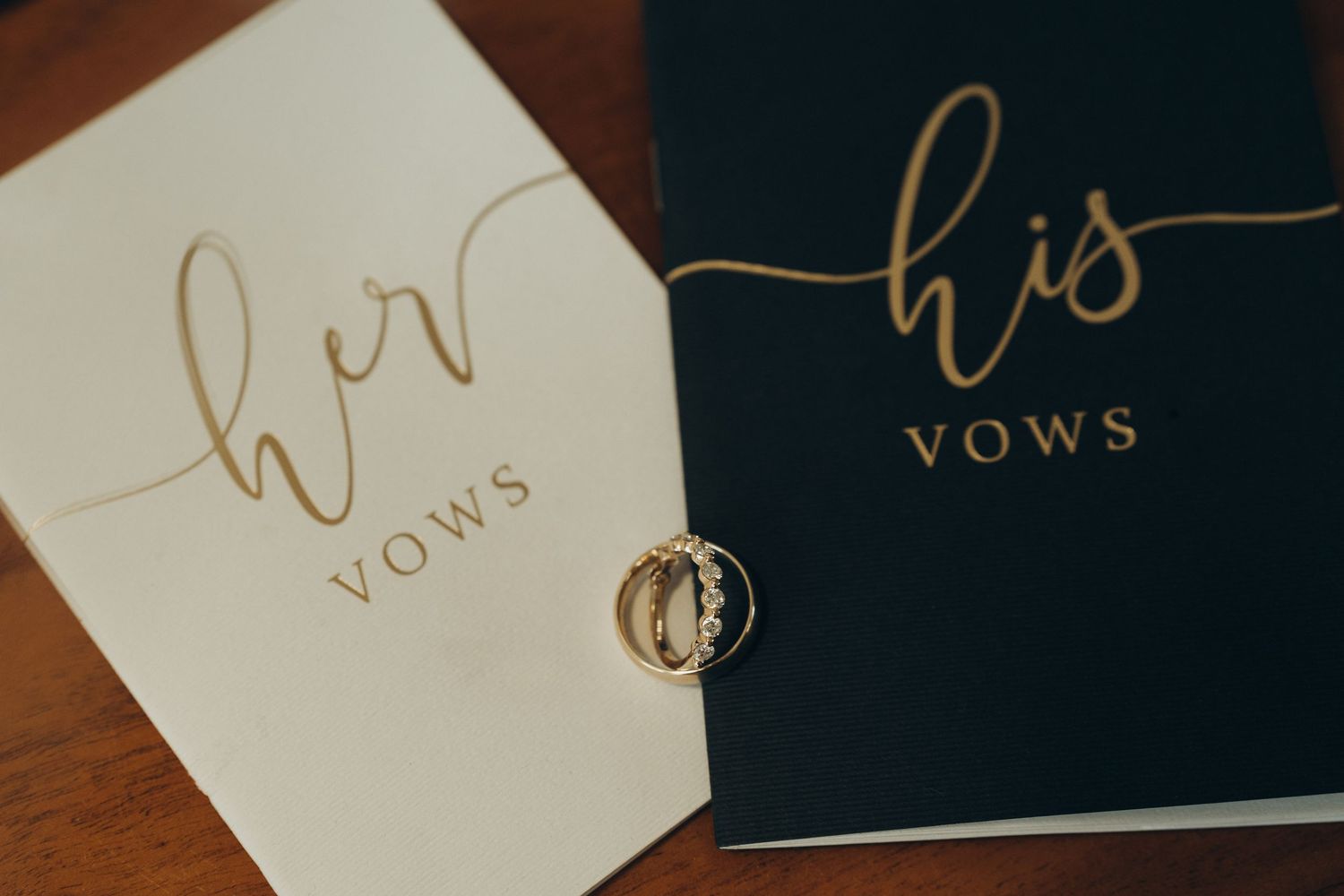 Elegant wedding vow books with gold foil lettering arranged on a dark wooden surface.