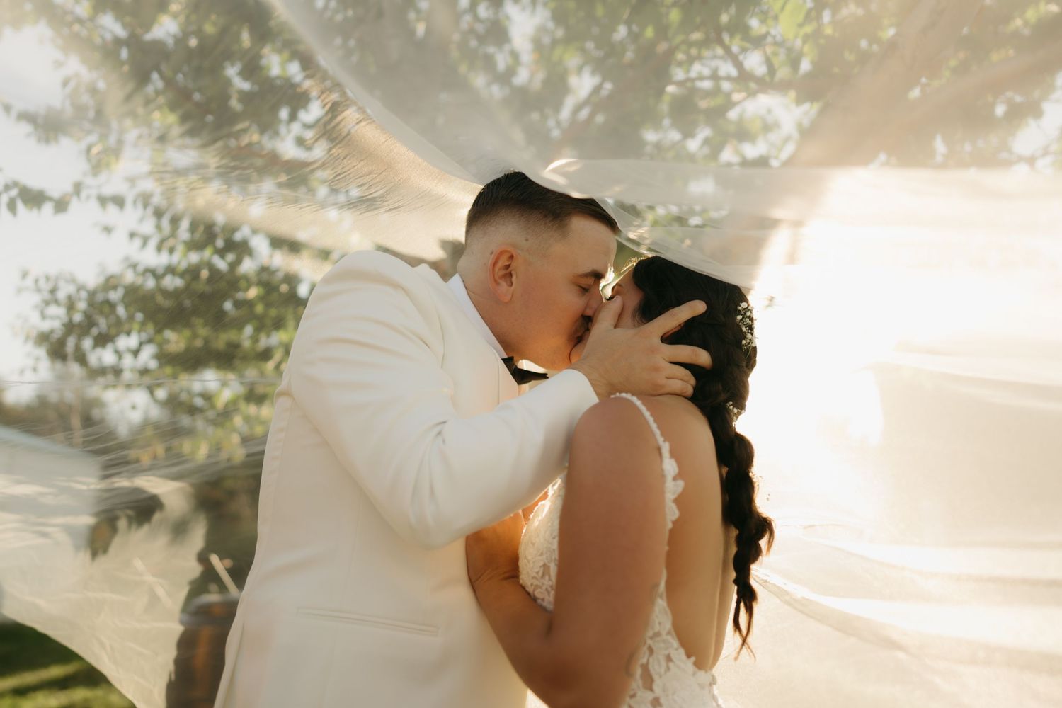 A romantic wedding couple shares intimate moments in a sunlit outdoor setting during their photo session.