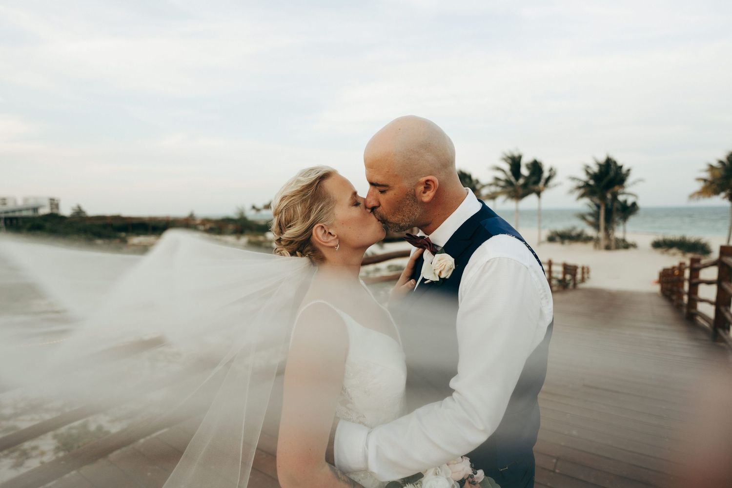 A dreamy beachside wedding scene with palm trees and soft clouds in the background.