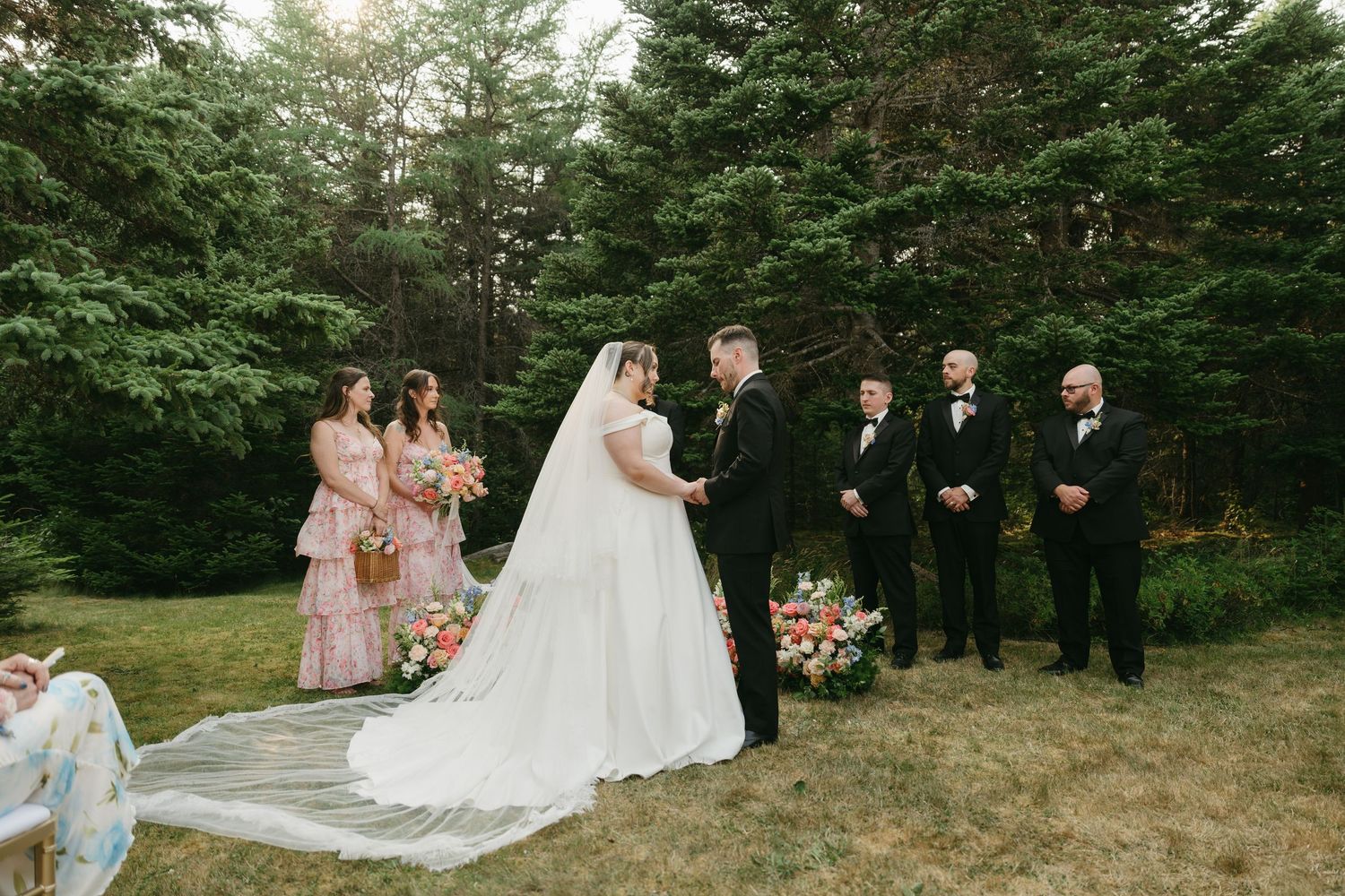 Wedding party gathered for outdoor photos with pine forest backdrop and natural lighting.