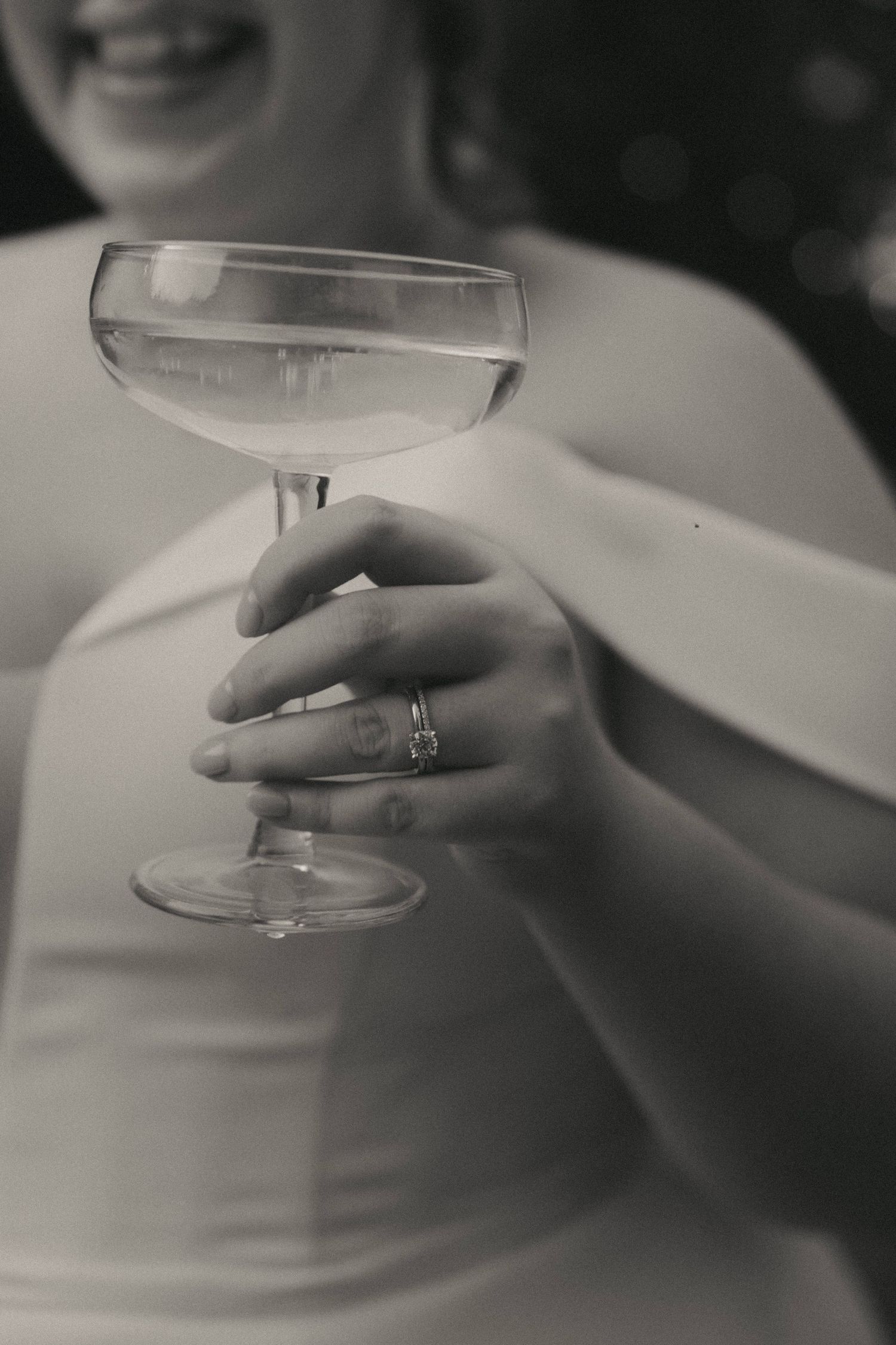 Close-up shot of a champagne glass held by a hand with an engagement ring.