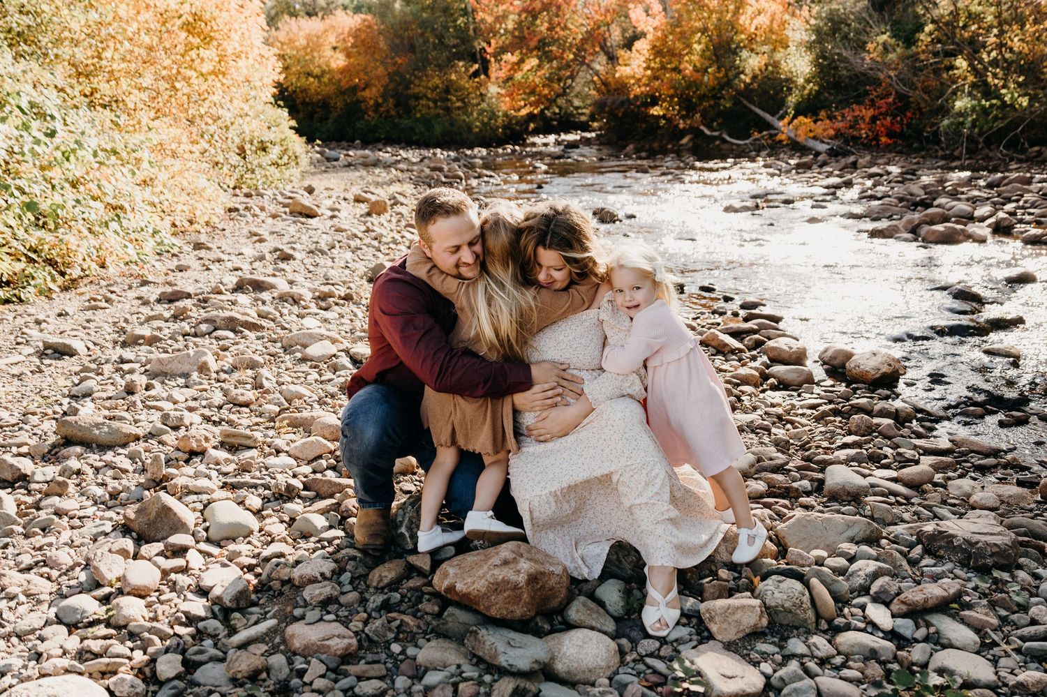 Family photography session on a rocky riverbank surrounded by natural scenery.