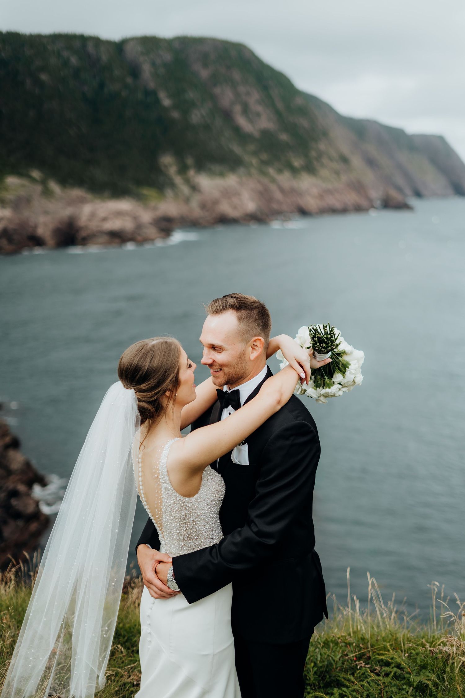 Wedding couple standing by dramatic coastal cliffs overlooking an ocean bay.