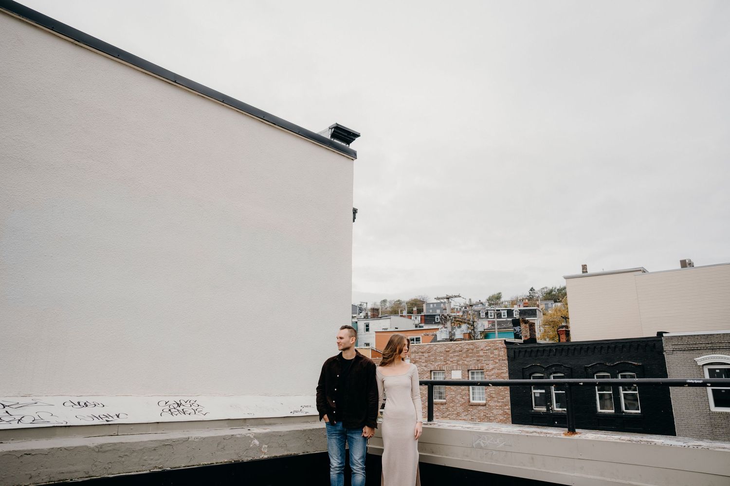 A rooftop view of an urban neighborhood with brick buildings and white walls against an overcast sky.