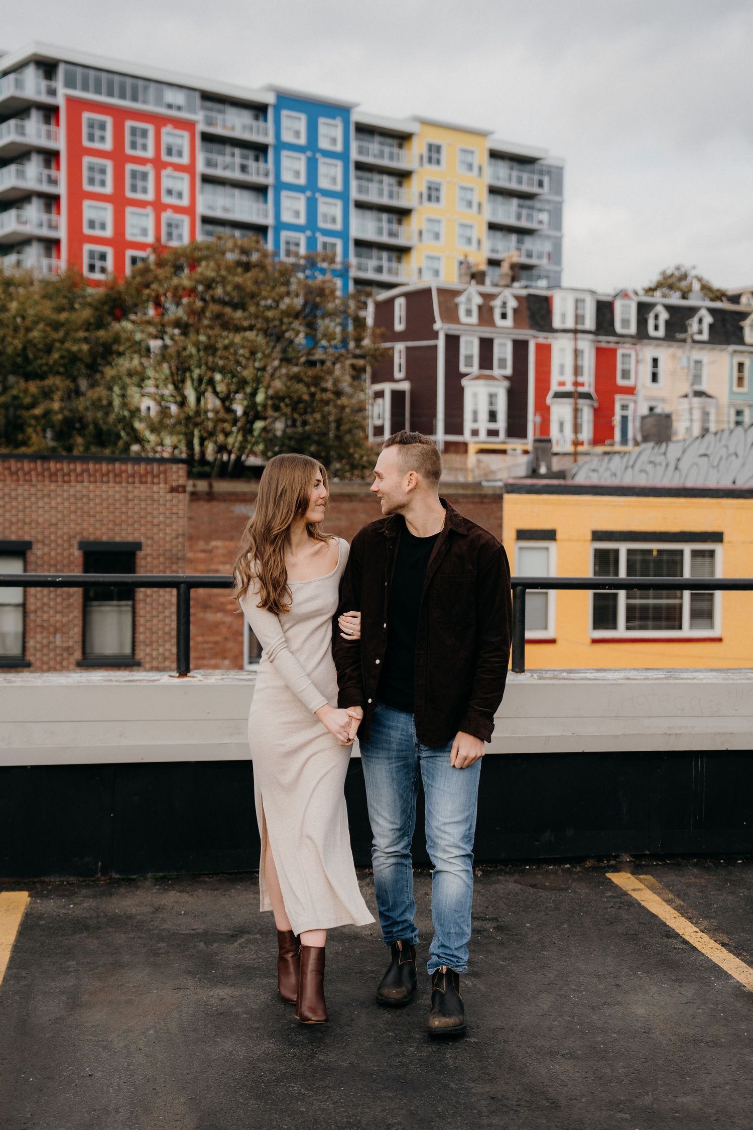 Couple sharing tender moments during rooftop photoshoot with urban cityscape backdrop.