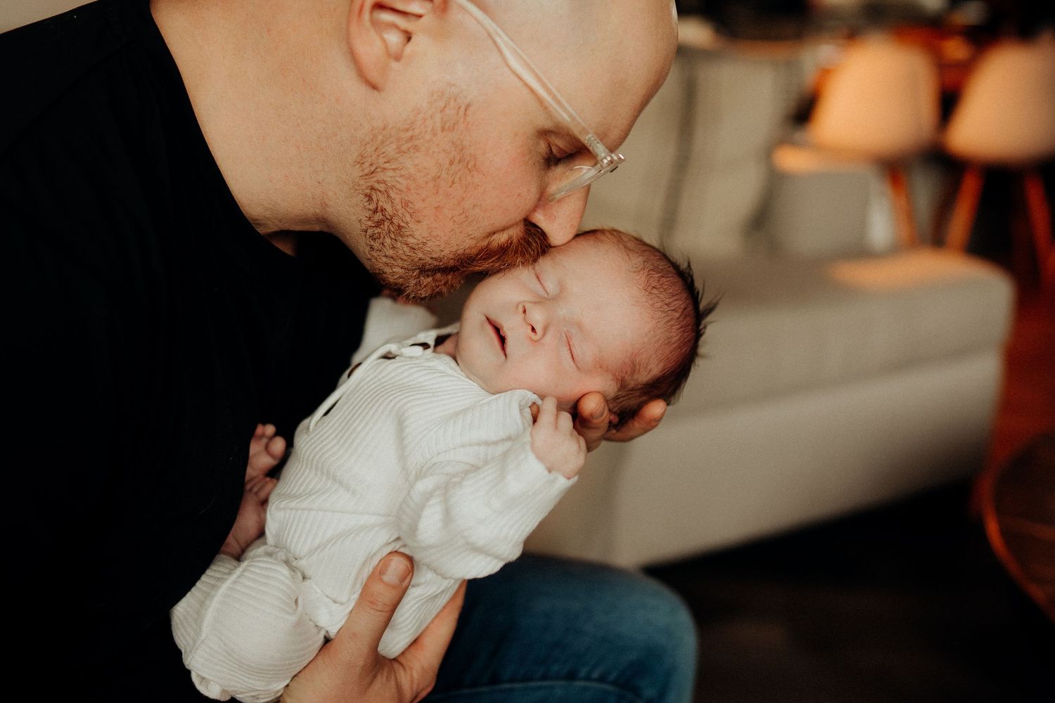 Family bonding with their newborn baby in cozy living room with soft window light.