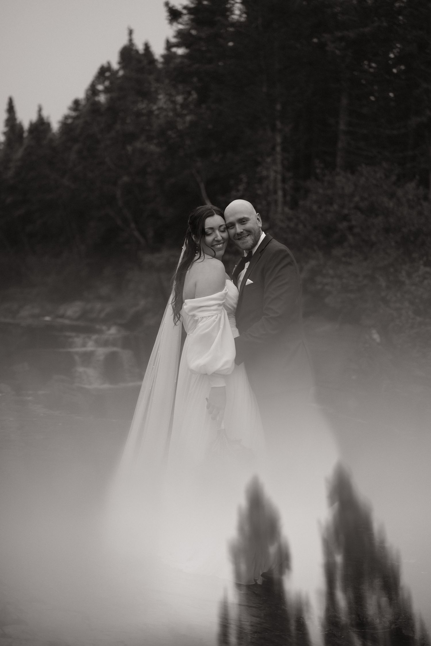 Romantic wedding couple embraces in dreamy forest setting with ethereal fog creating a mystical atmosphere.