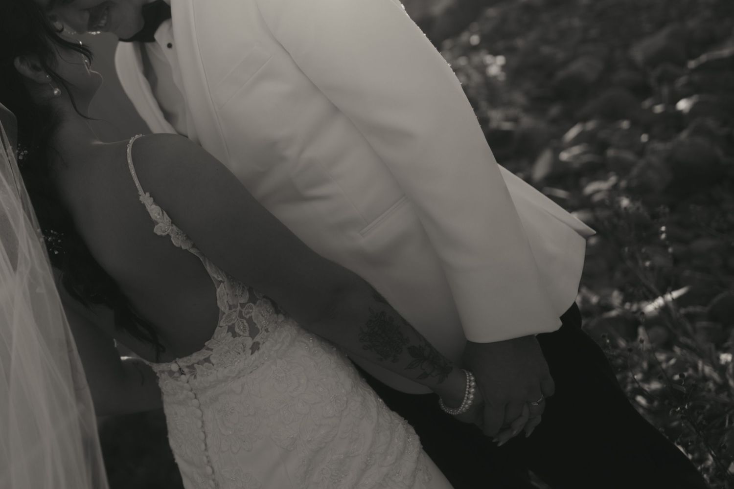 A black and white photograph shows a person in a white wedding dress walking through an outdoor garden setting.