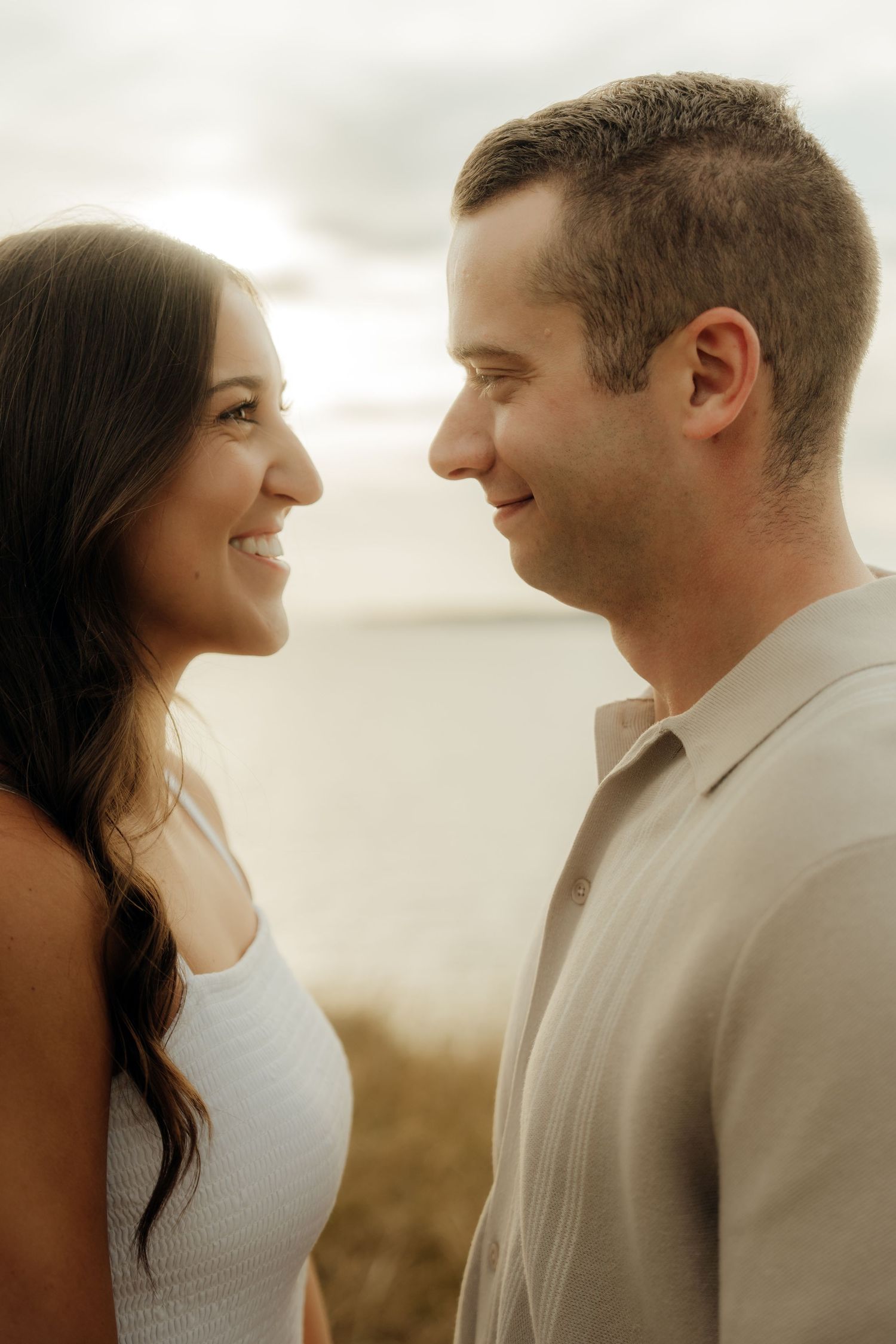 A couple shares an intimate moment smiling at each other during a golden hour outdoor photo session.