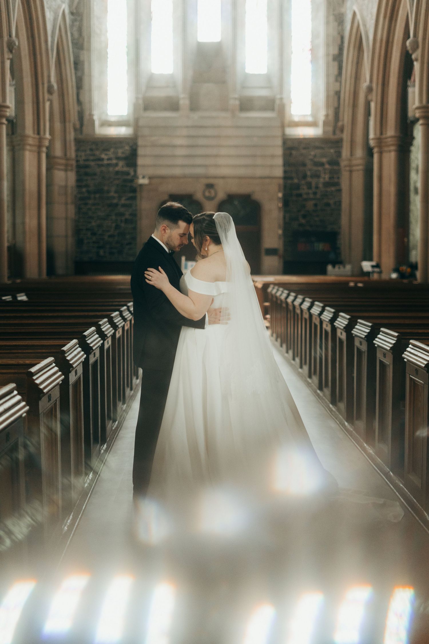 Intimate wedding portrait in a cathedral with sunlight streaming through stained glass windows.