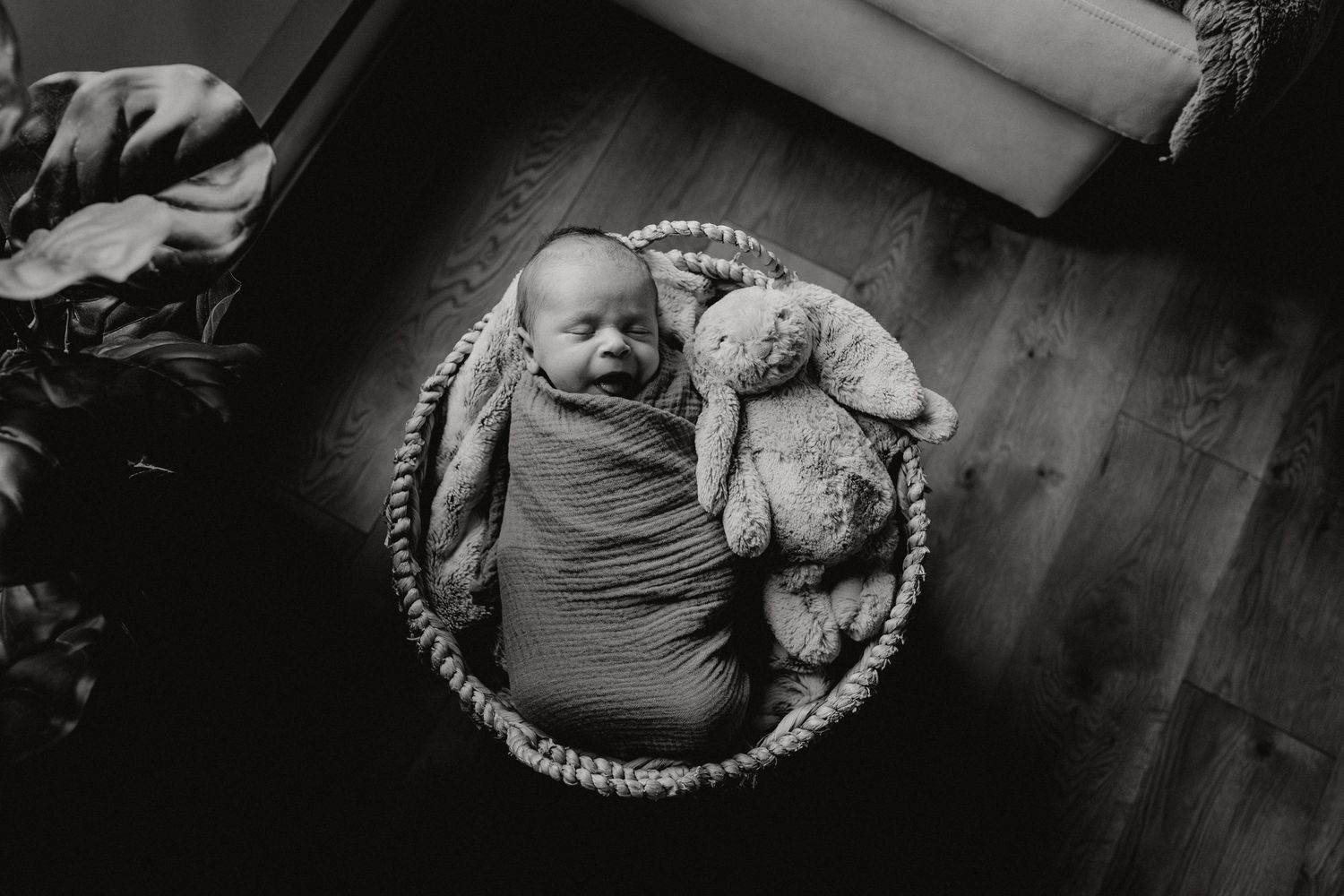 Moody black and white photo of sleeping baby in woven basket.