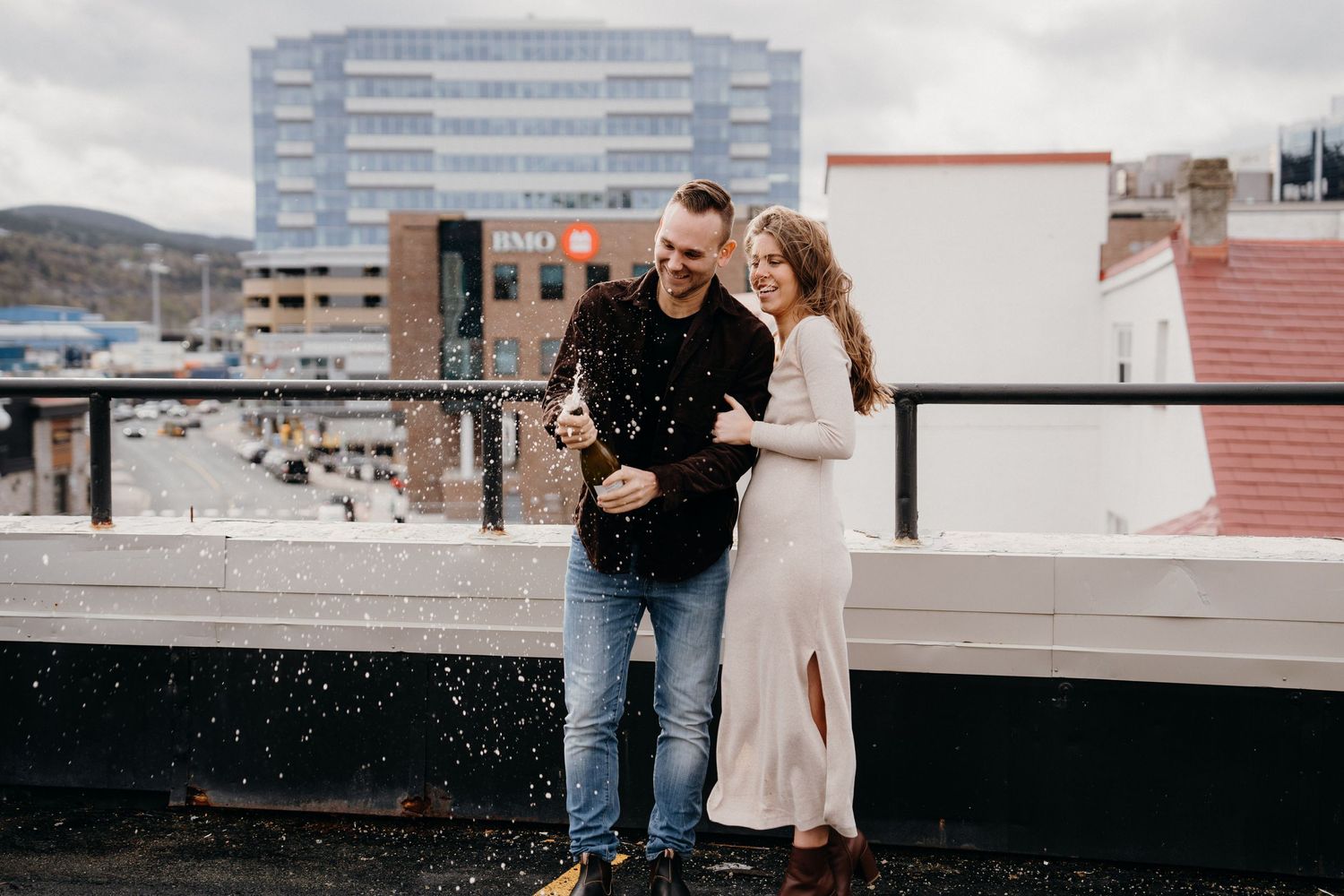 A couple shares a romantic moment on an urban rooftop with city buildings in the background.