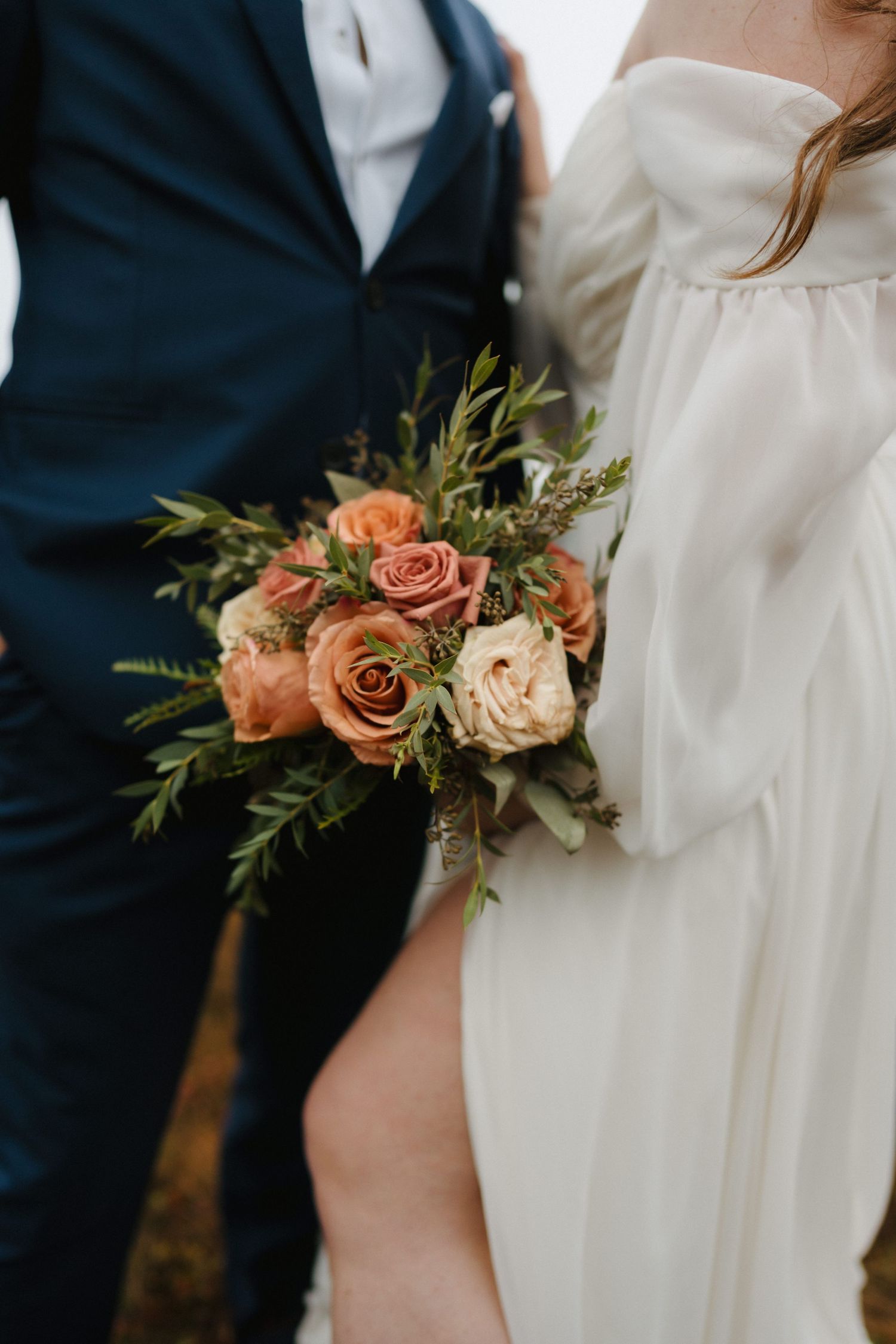 A close-up detail of a wedding couple showing navy suit jacket next to white dress with peach and blush floral accents.
