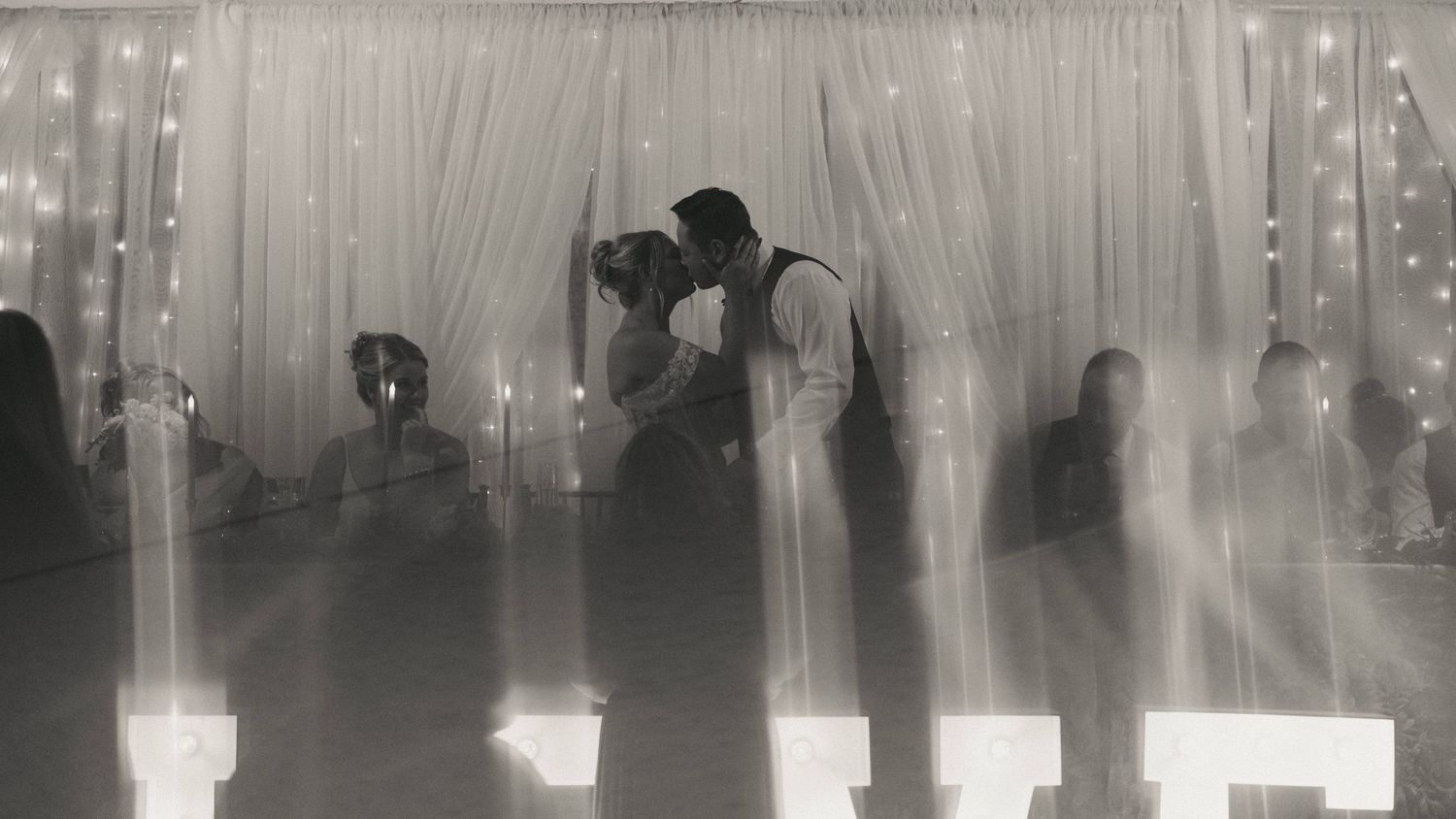 Black and white photo of a couple sharing their first dance at a wedding reception with candlelit backdrop.