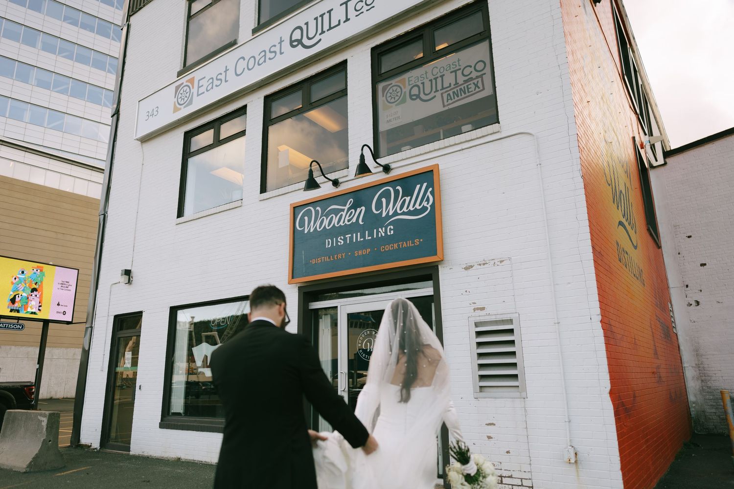 Bride and groom holding hands outside Wooden Walls Distilling and East Coast Quiltes on their wedding day.