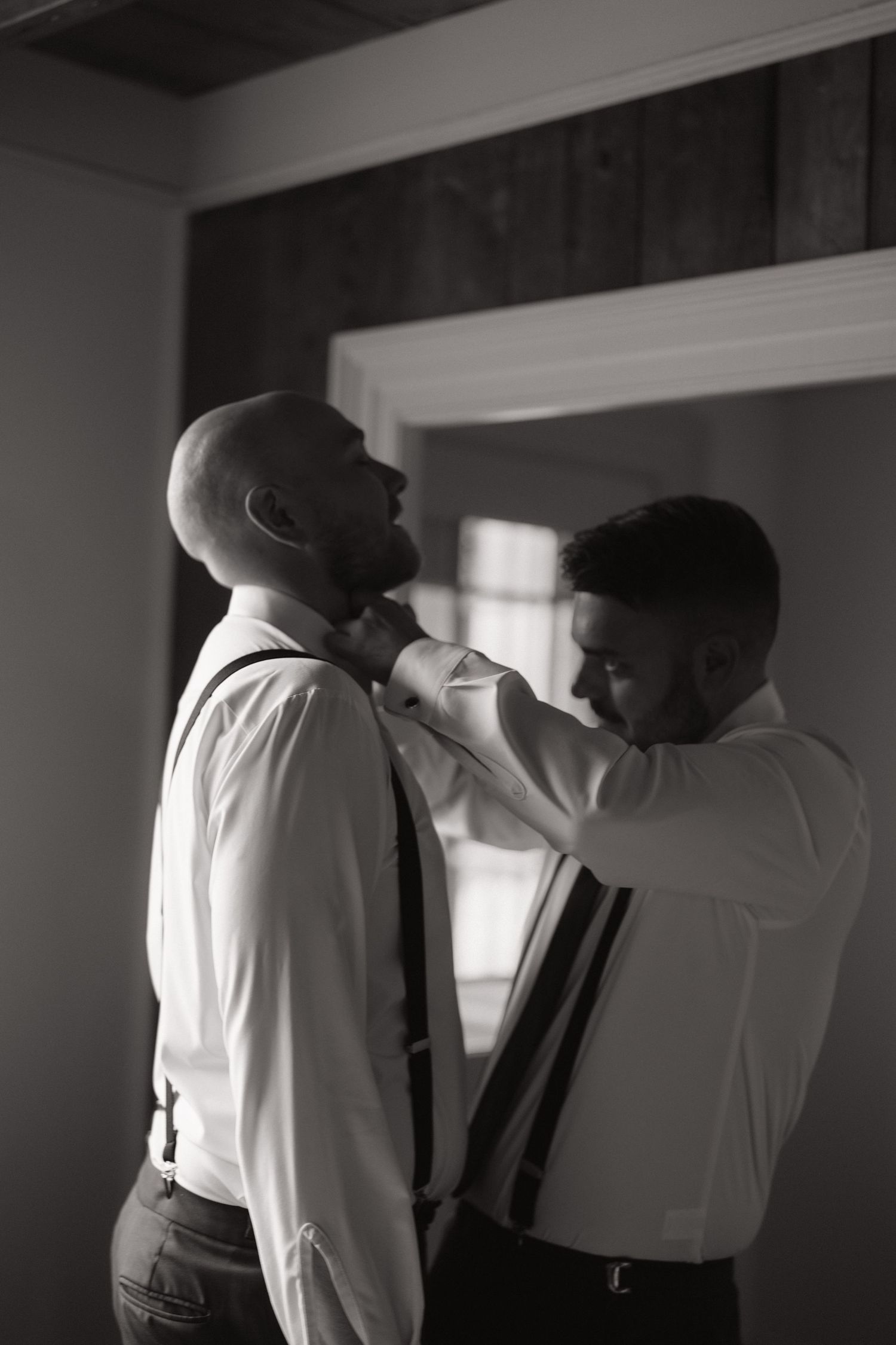 A black and white sequence of four images showing two men in formal attire interacting in a dimly lit room.