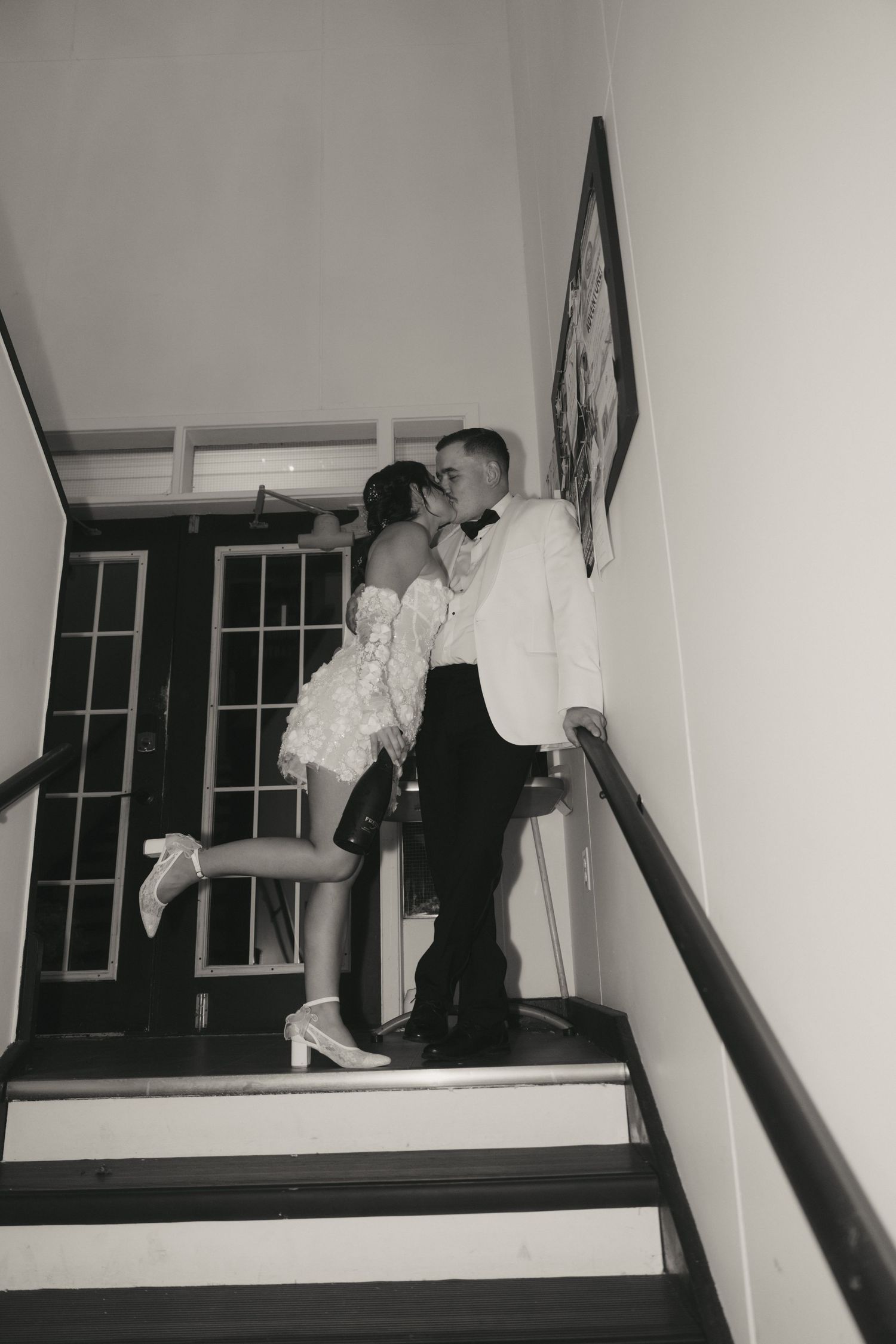 A romantic black and white photo of a couple embracing on a staircase with French doors visible in the background.