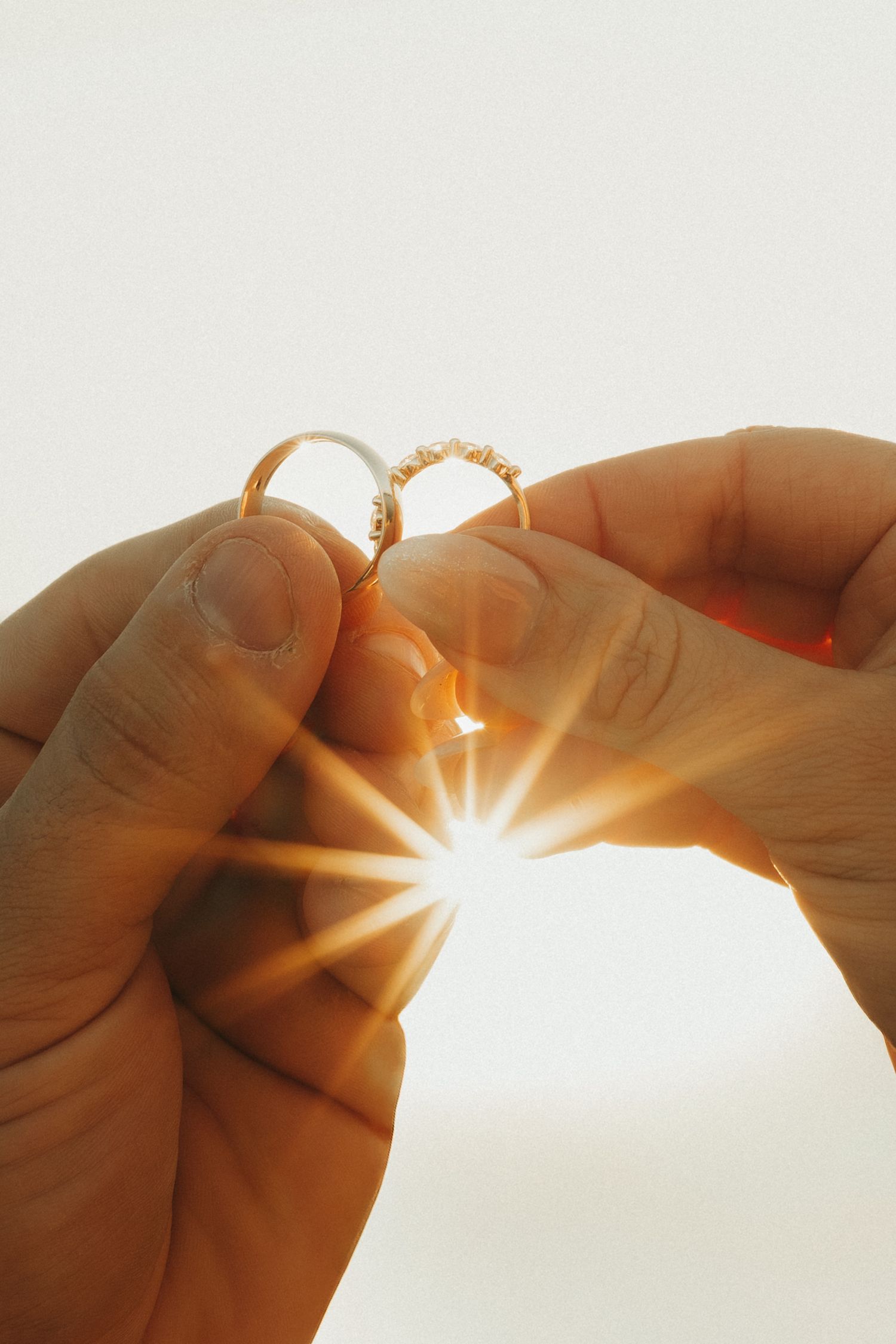 Hands holding a delicate gold ring up to sunlight creating a beautiful starburst effect through the jewelry.