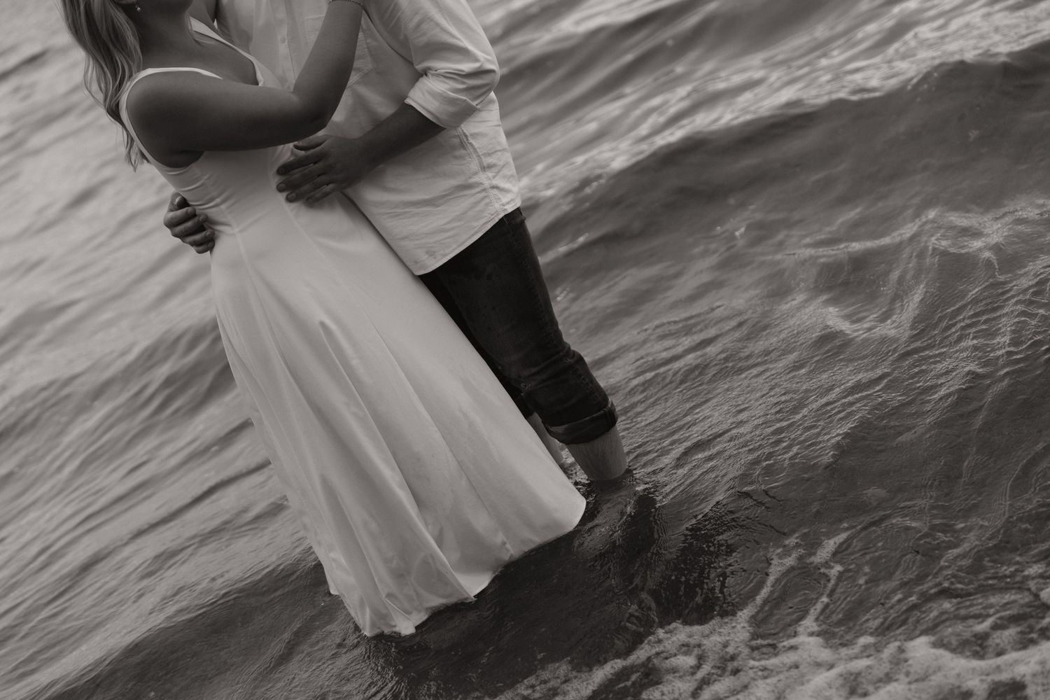 Black and white wedding photos show couple walking along rocky beach shoreline in formal attire.