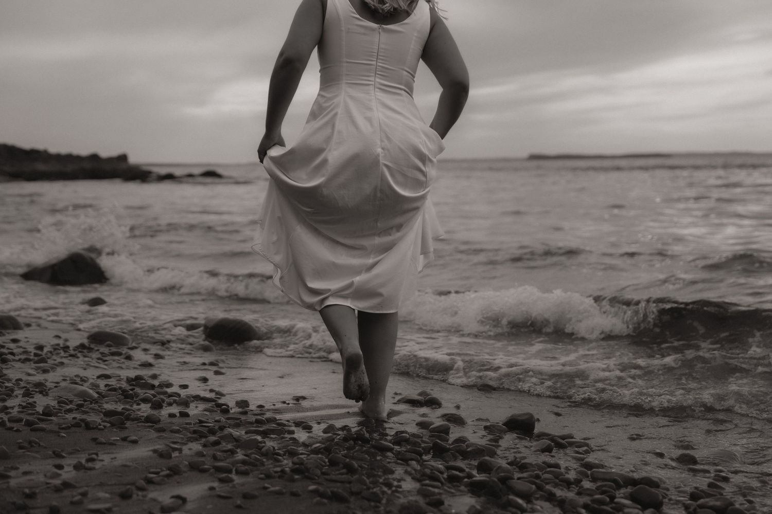 Black and white photos of a couple walking along a rocky beach shoreline at sunset.