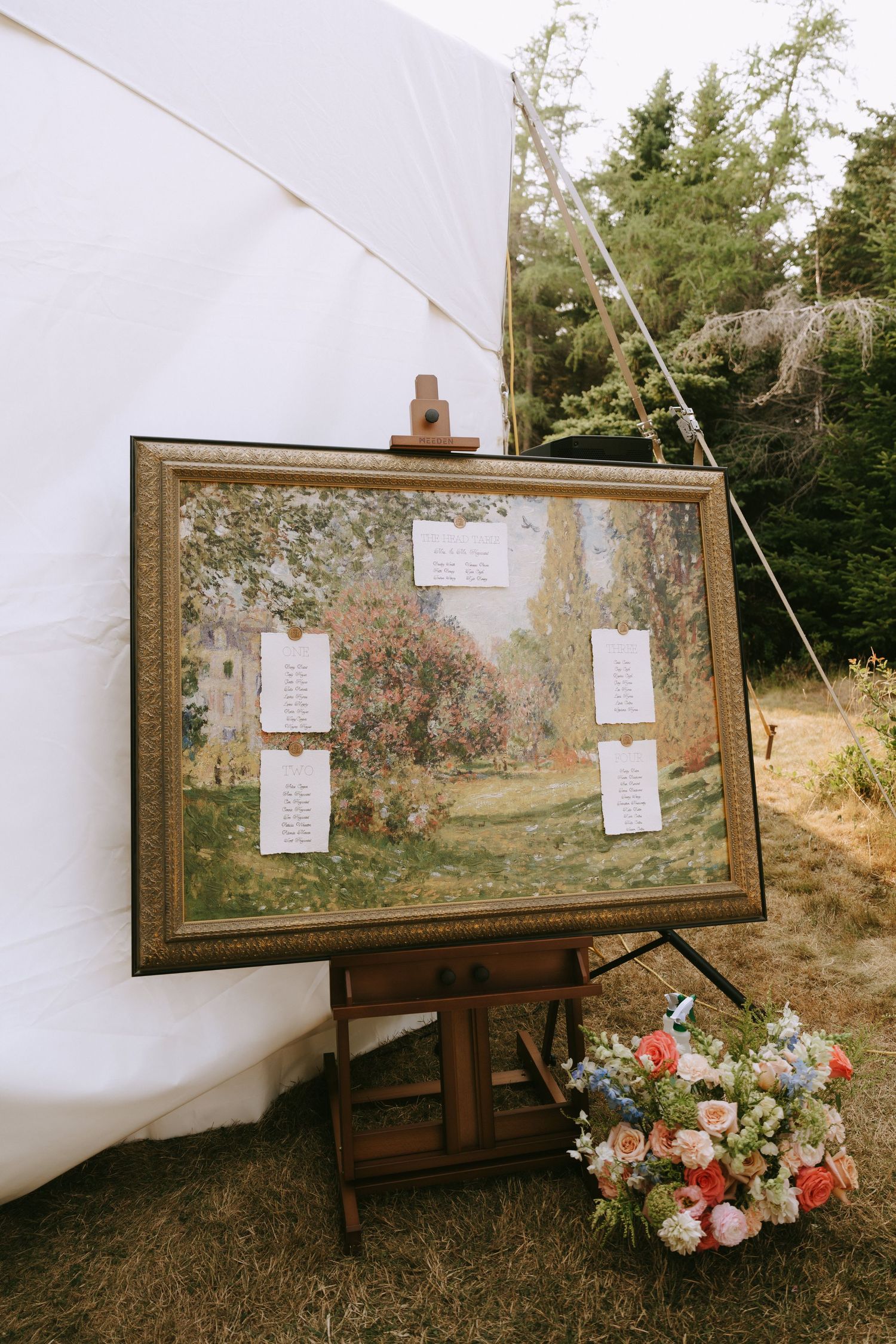 Framed artwork display against white backdrop with floral arrangements in an outdoor setting.