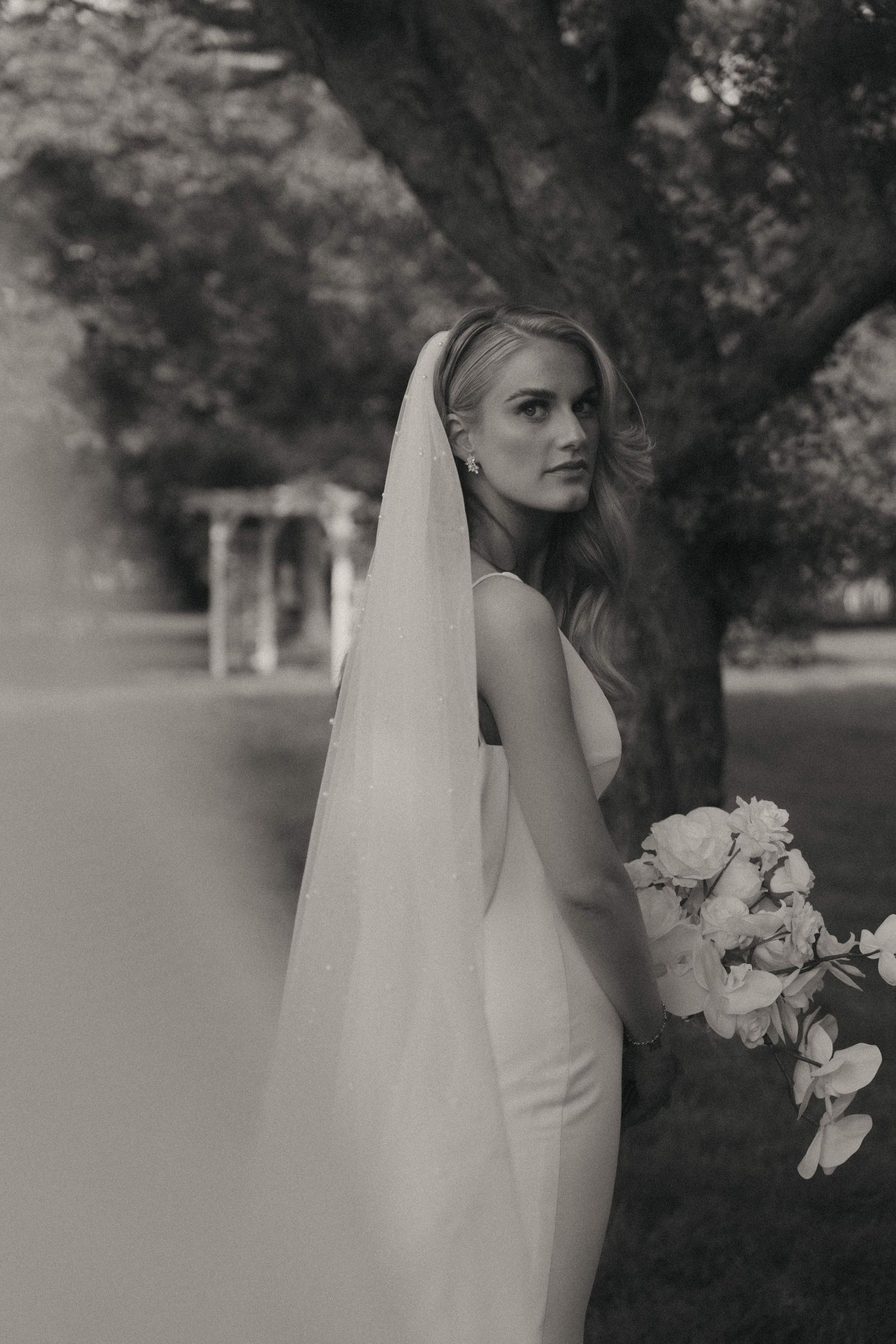 Classic bridal portrait showing flowing white gown and veil against natural outdoor backdrop.