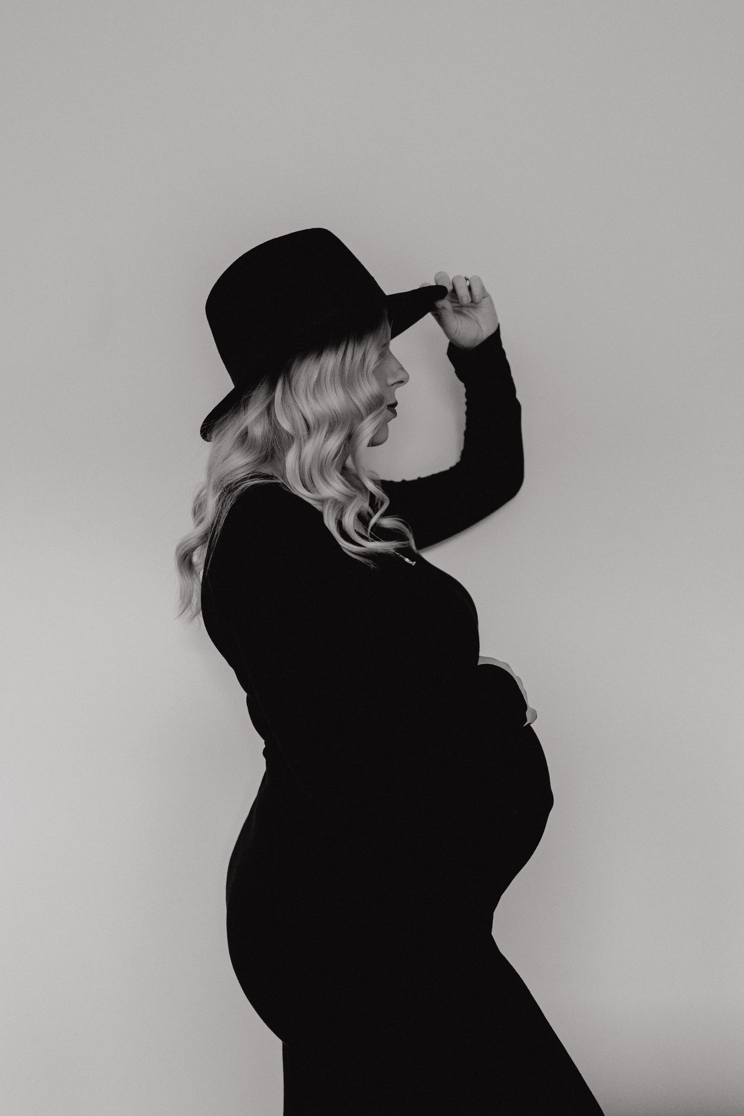 Silhouetted figure in dark clothing poses against light background in artistic black and white portrait series.