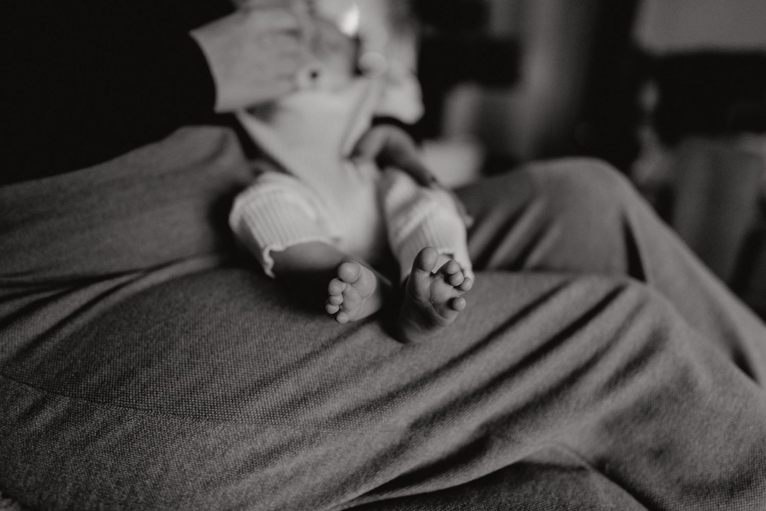 Small feet and legs of a baby resting on dark fabric in monochrome.