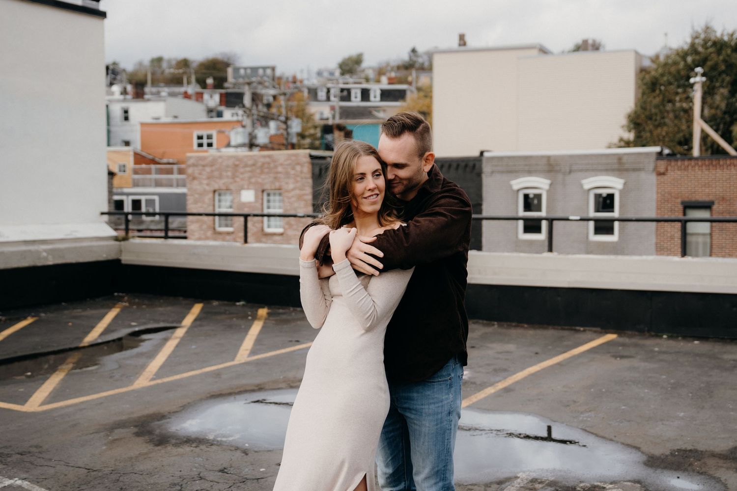Couple shares affectionate embrace during rooftop portrait session with city views.