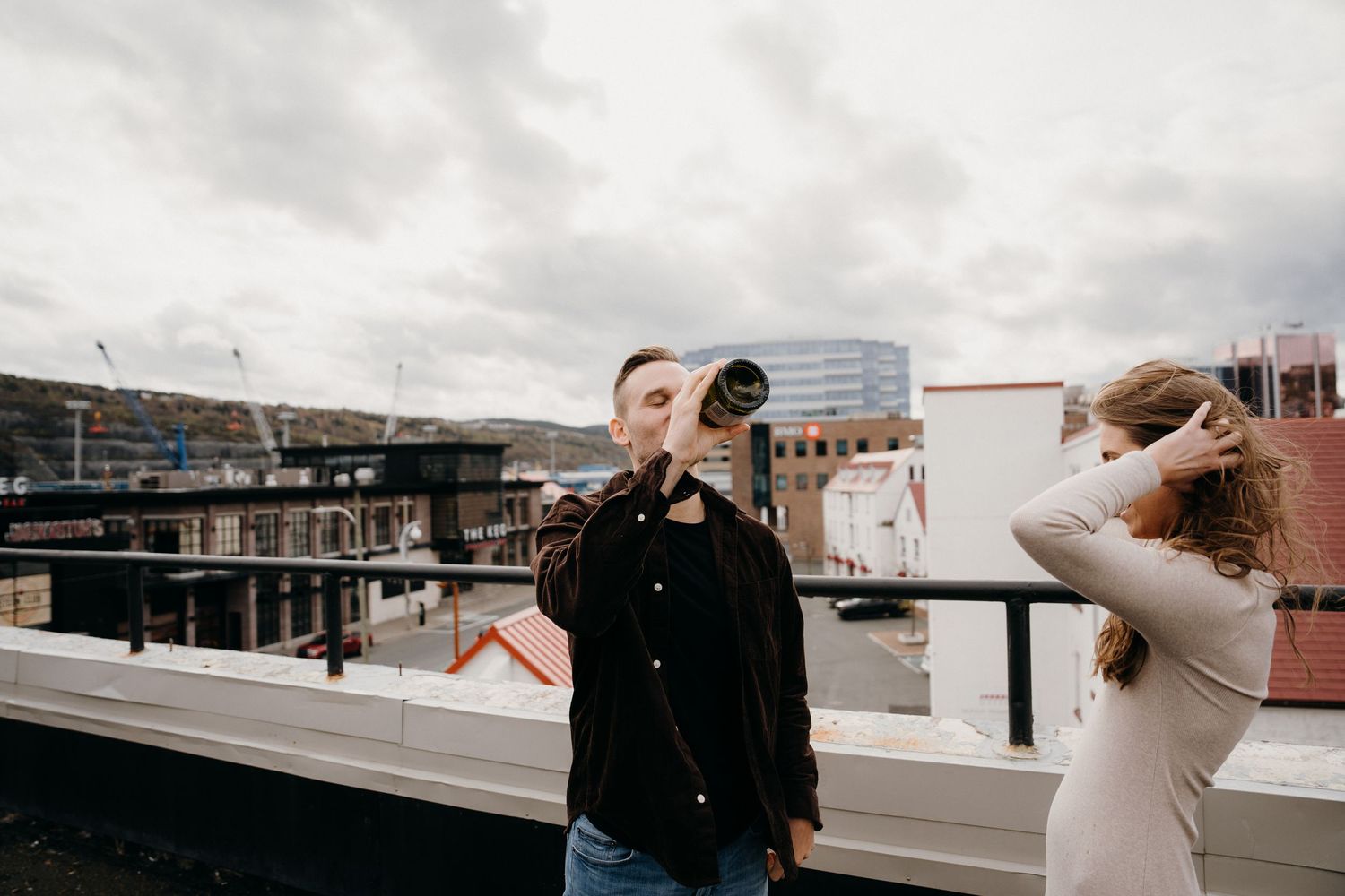 Couple enjoying drinks together on an urban rooftop balcony on a cloudy day.