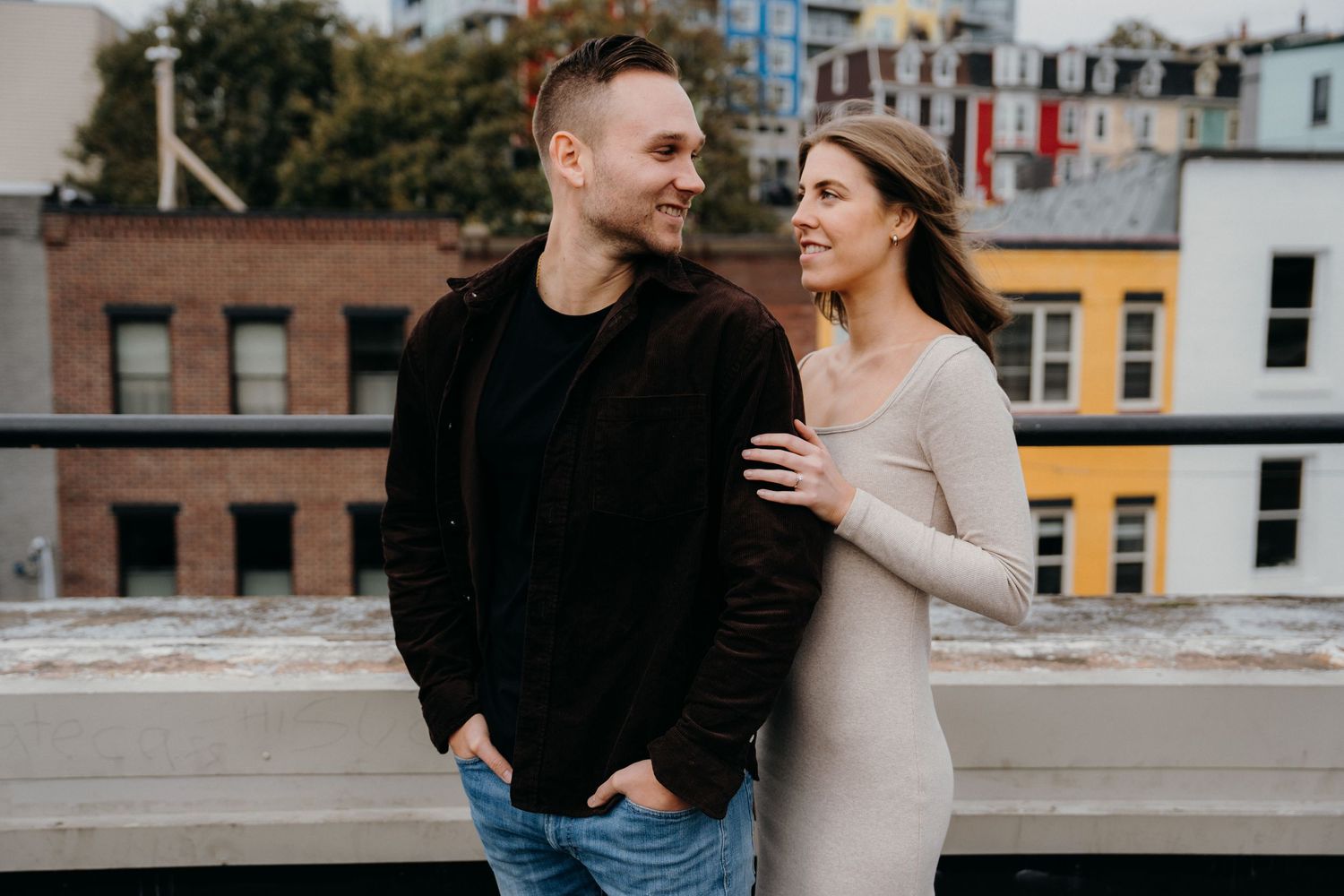 Couple embracing on urban rooftop with colorful apartment buildings visible behind them.
