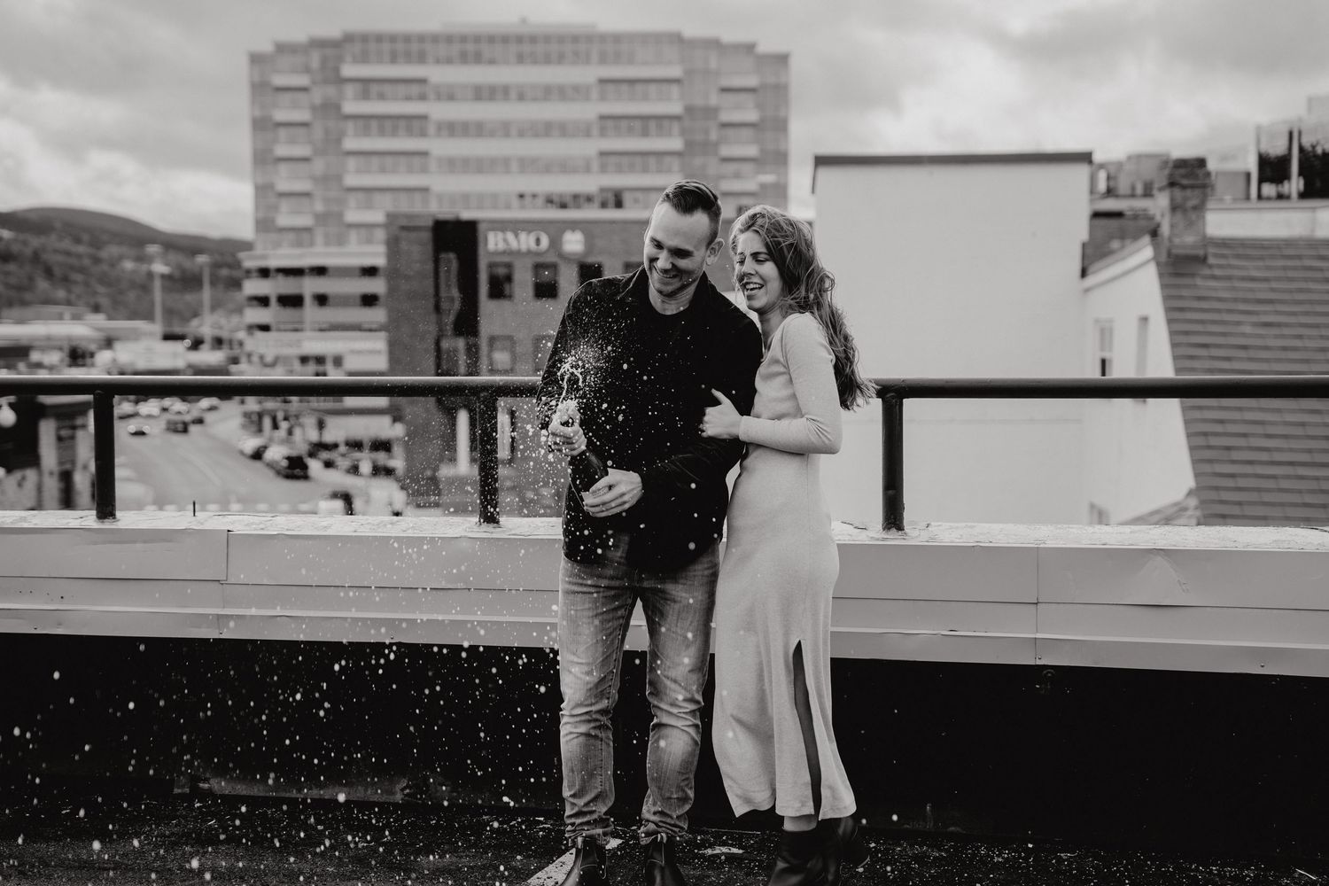 A couple shares a romantic moment on an urban rooftop with city buildings in the background.