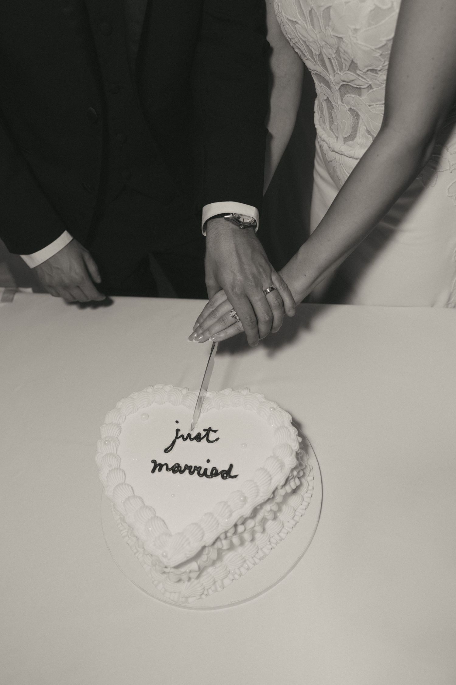 Newlyweds cutting a heart-shaped wedding cake inscribed with just married in black and white photo.